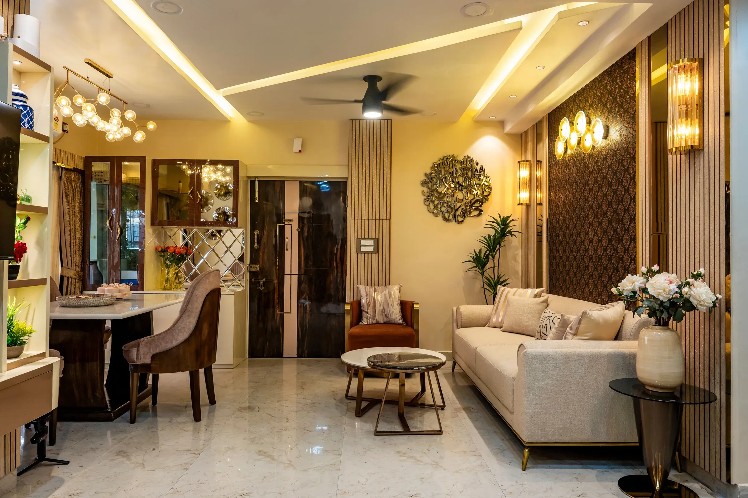 Indian living room with a cream sofa, fluted wooden panels, crystal wall sconces, metal wall art and dining corner