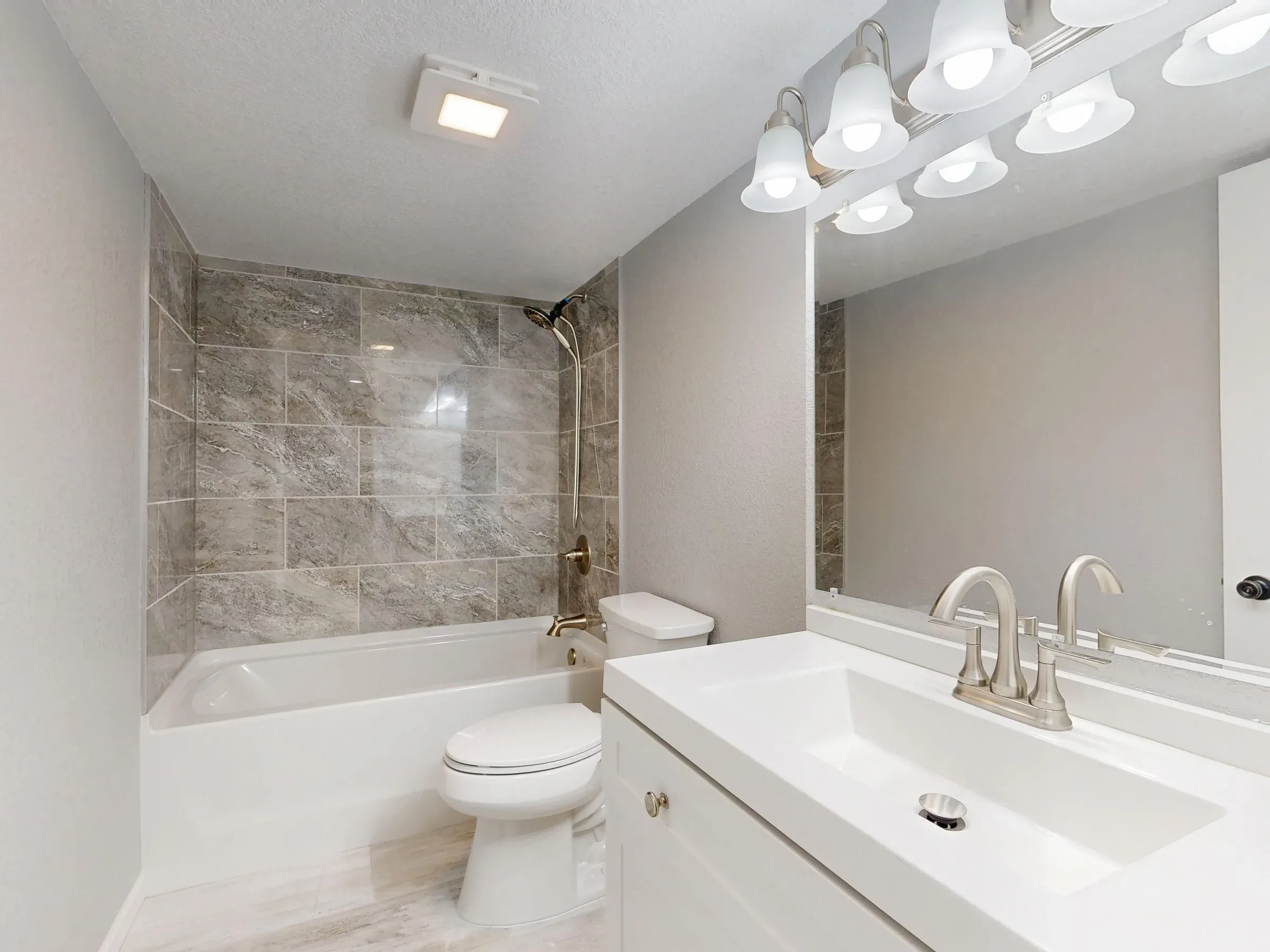 Simple bathroom with grey tiles around a bathtub-shower, a white vanity and vanity lights