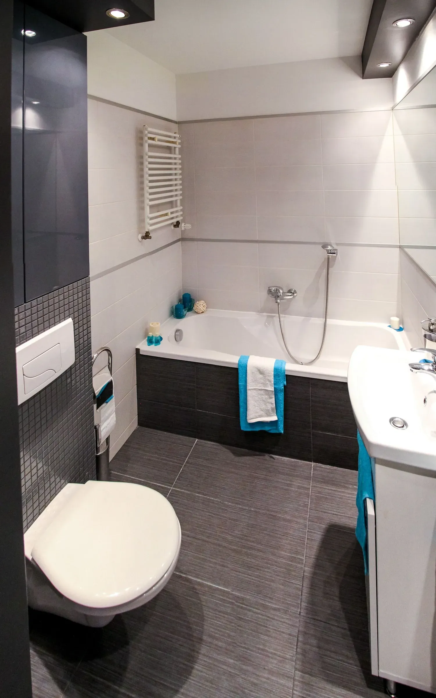 Small bathroom with white wall tiles, dark grey floor tiles and mosaic, a wall-hung WC and bathtub