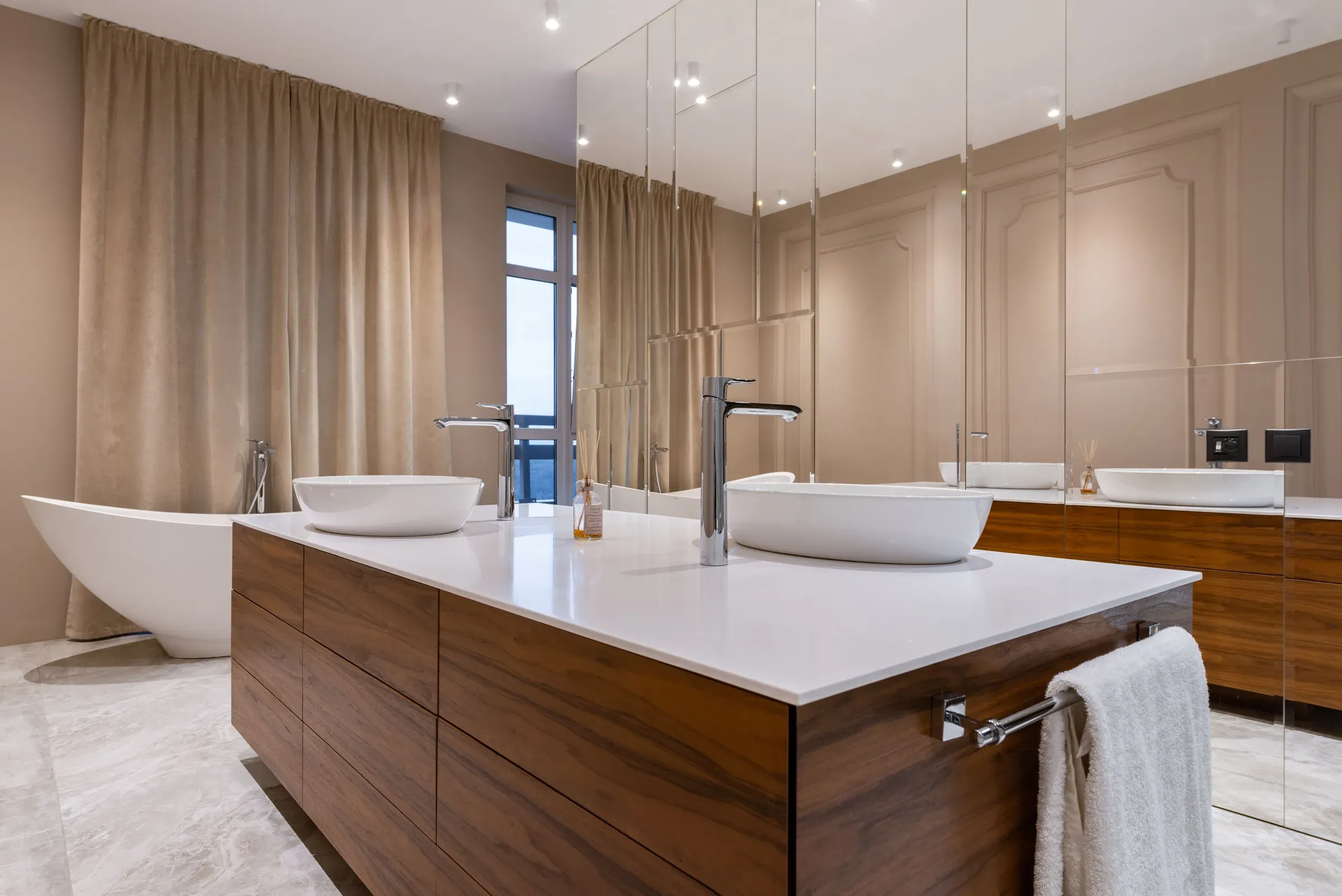 Luxury bathroom with a walnut island vanity, twin vessel basins, white quartz top, freestanding tub and mirrored wall