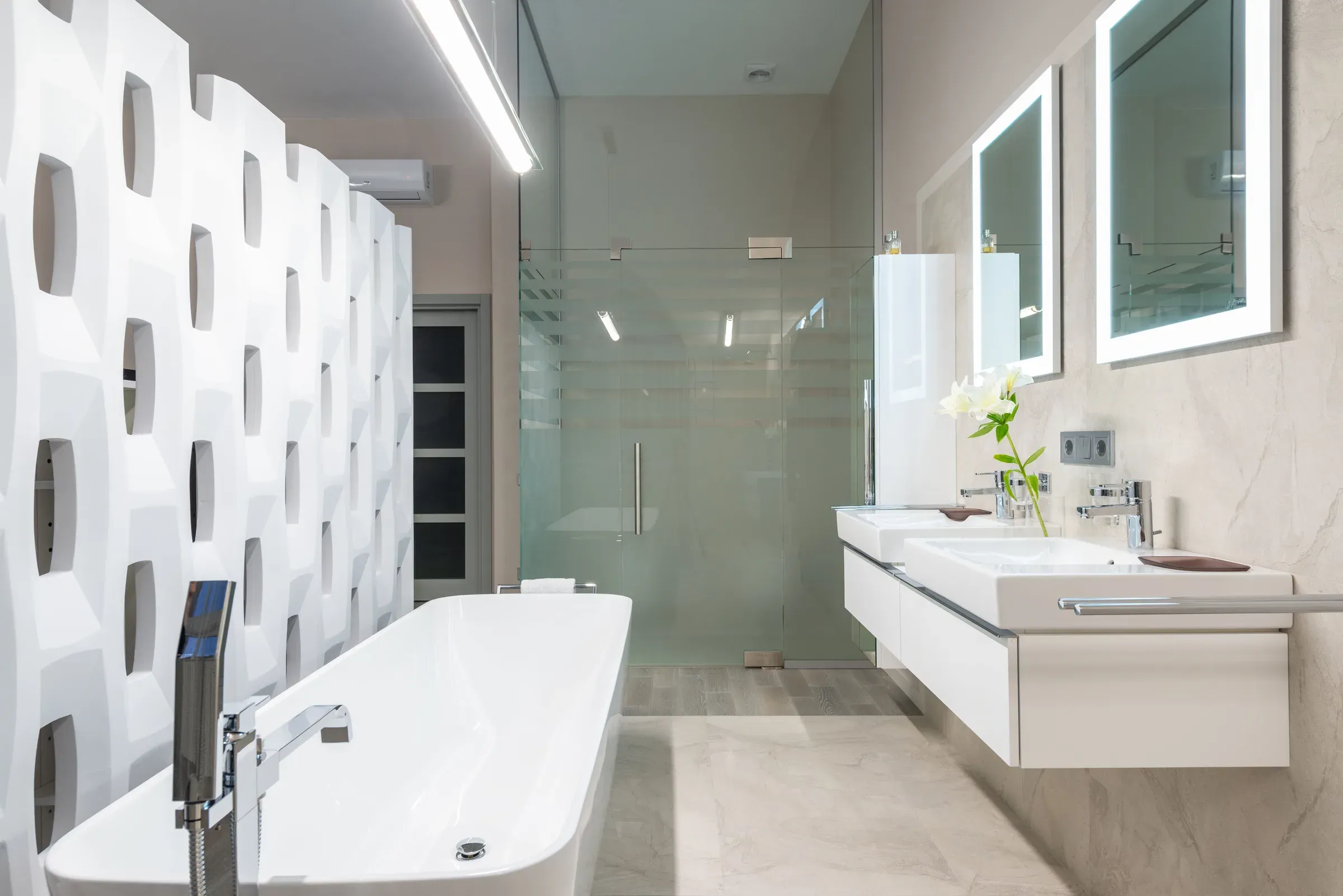 Bright white bathroom with a freestanding tub, sculpted 3D partition wall, double floating vanity and backlit mirrors