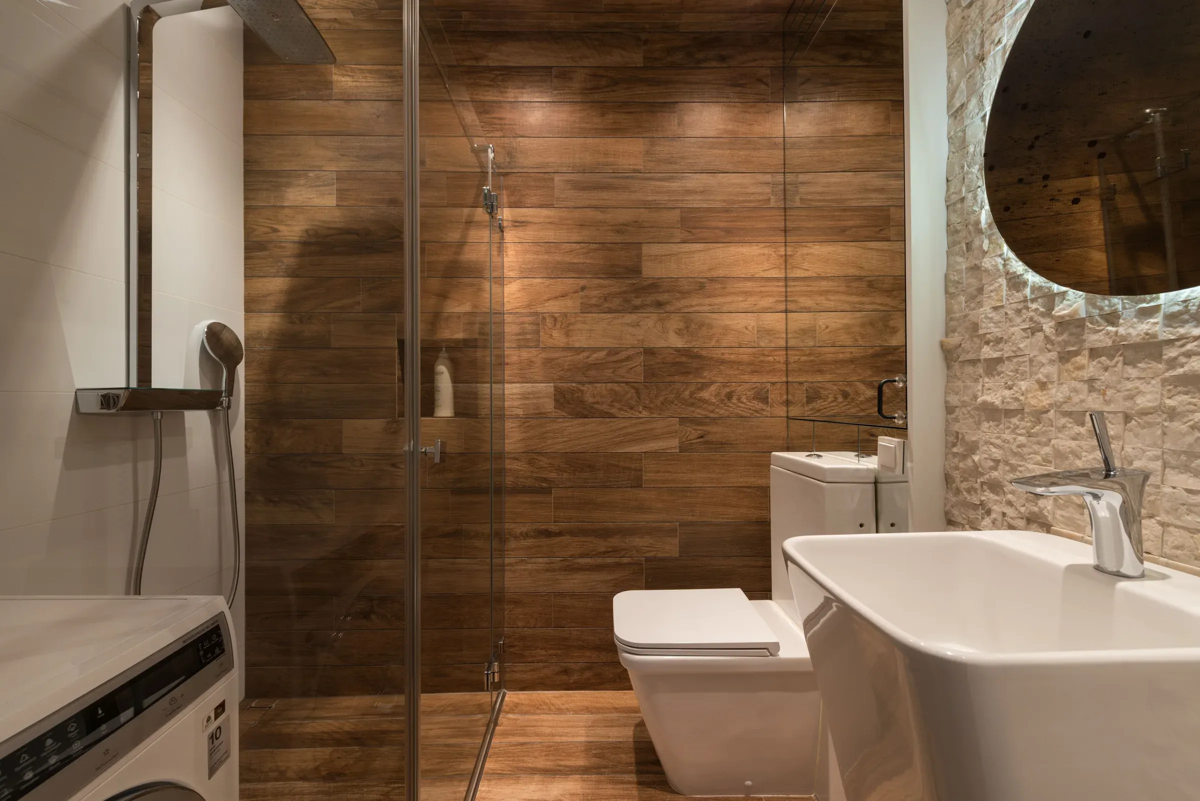 Bathroom with wood-look plank tiles in the shower, a glass partition, stone-cladding wall and a round backlit mirror