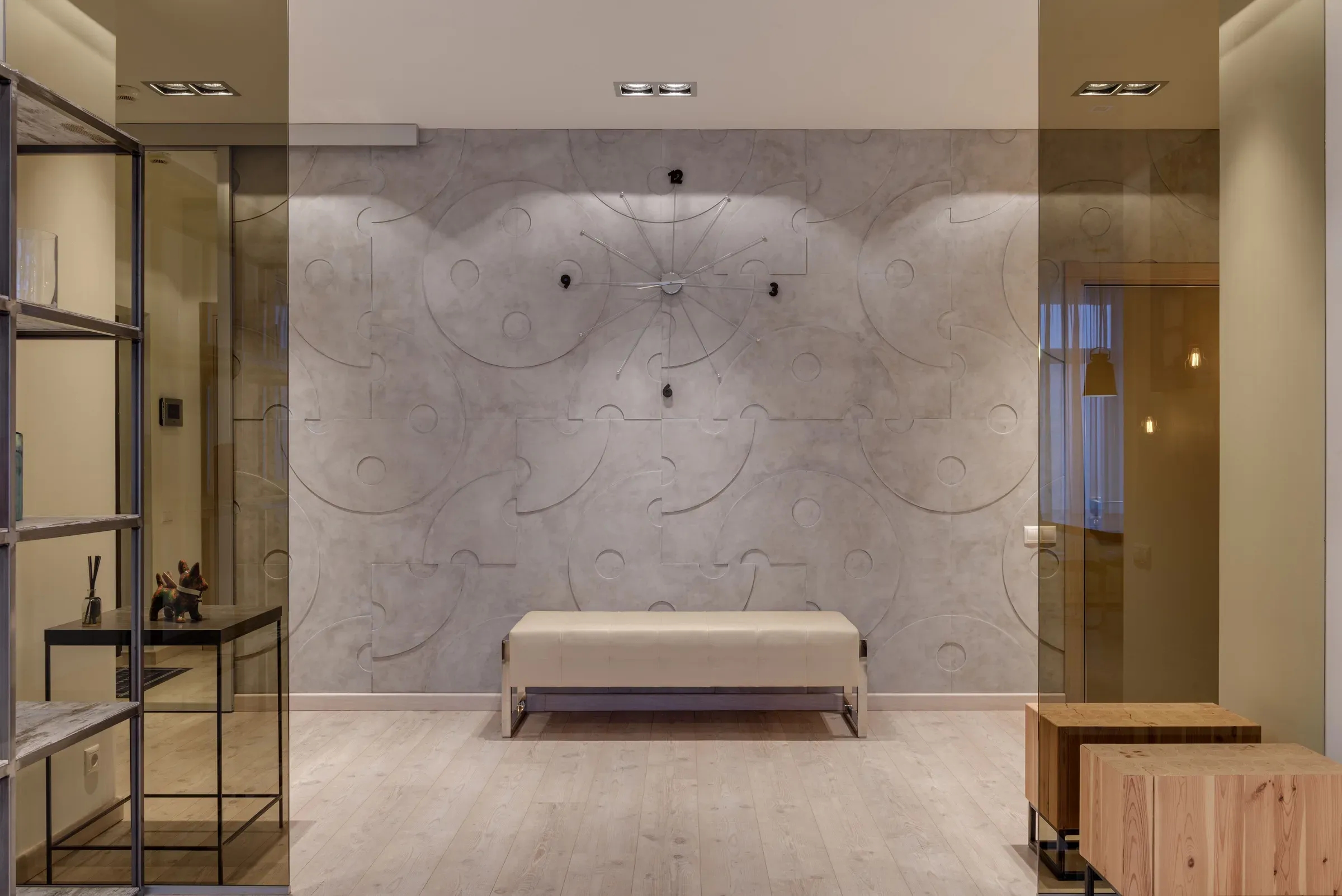 Foyer with a sculpted grey relief wall, upholstered bench, glass partitions and wooden stools