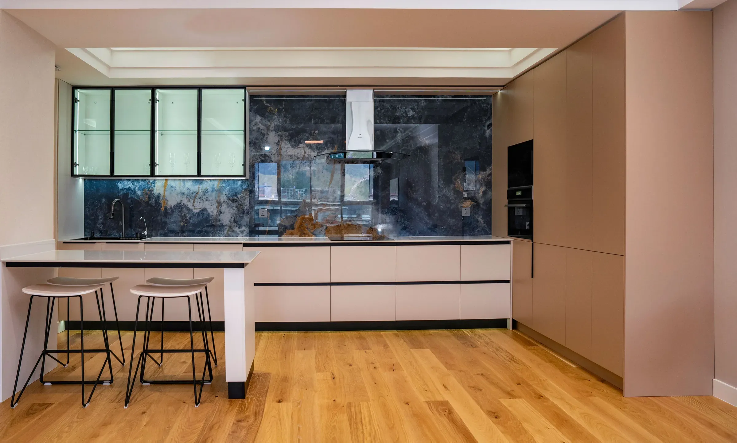 Kitchen with a dark marble backsplash, blush handleless cabinets, chimney and a breakfast counter with stools