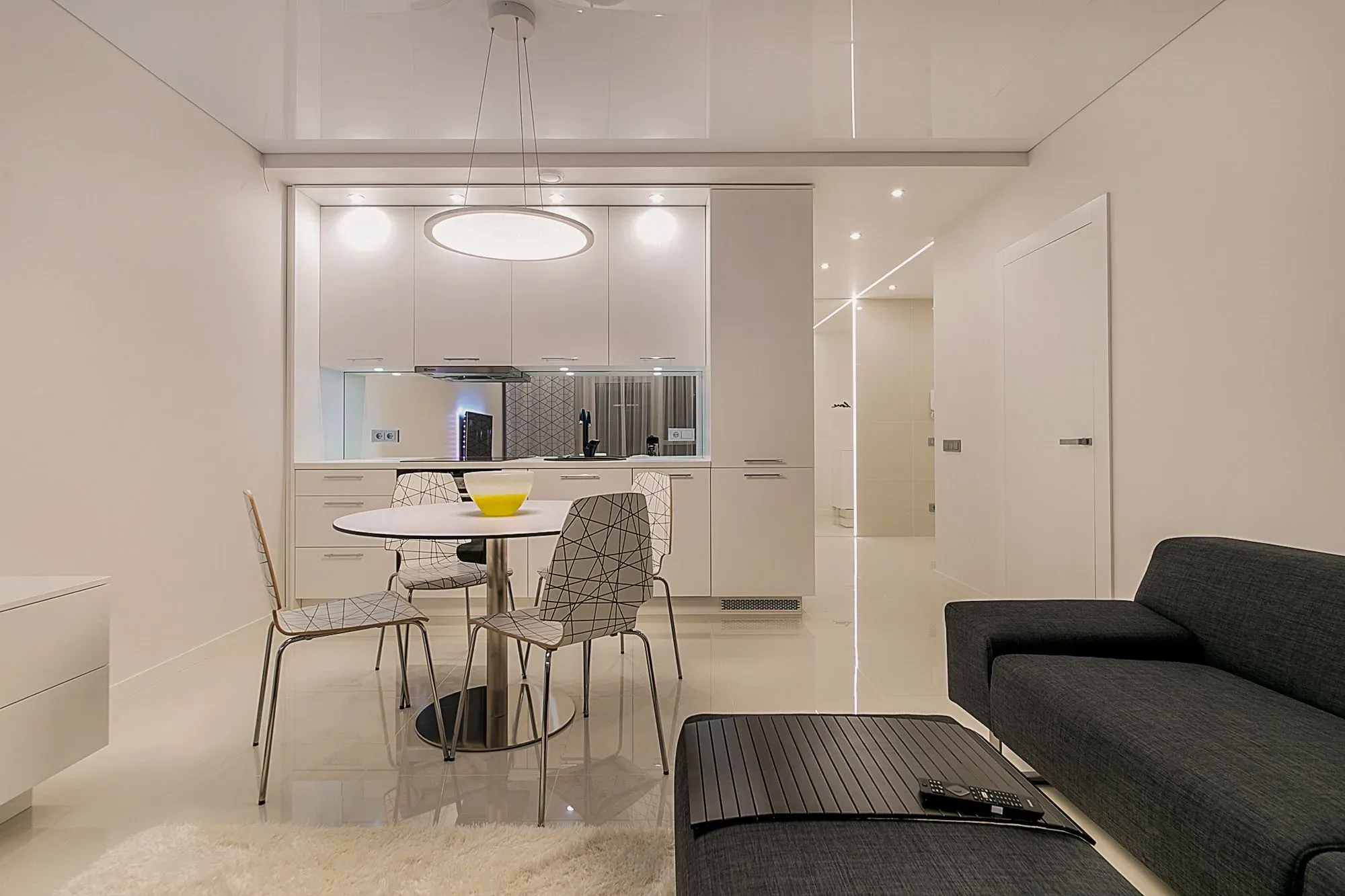 White gloss kitchen with a round dining table, ring pendant light and a dark sofa in the foreground