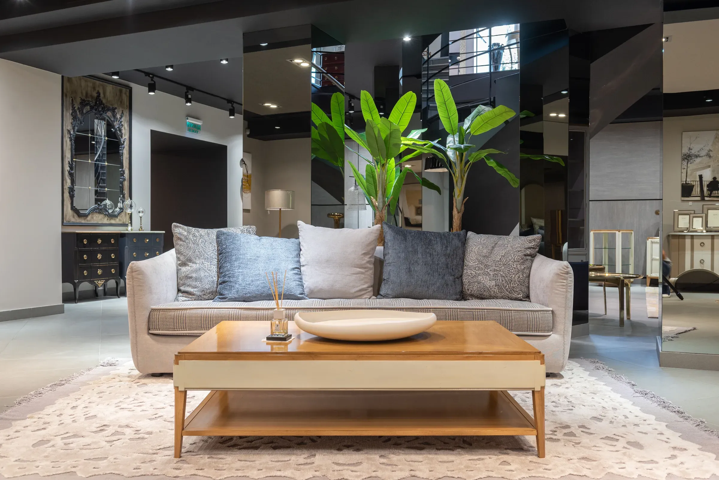 Beige sofa with grey cushions, a wooden coffee table, plants and dark mirrored walls