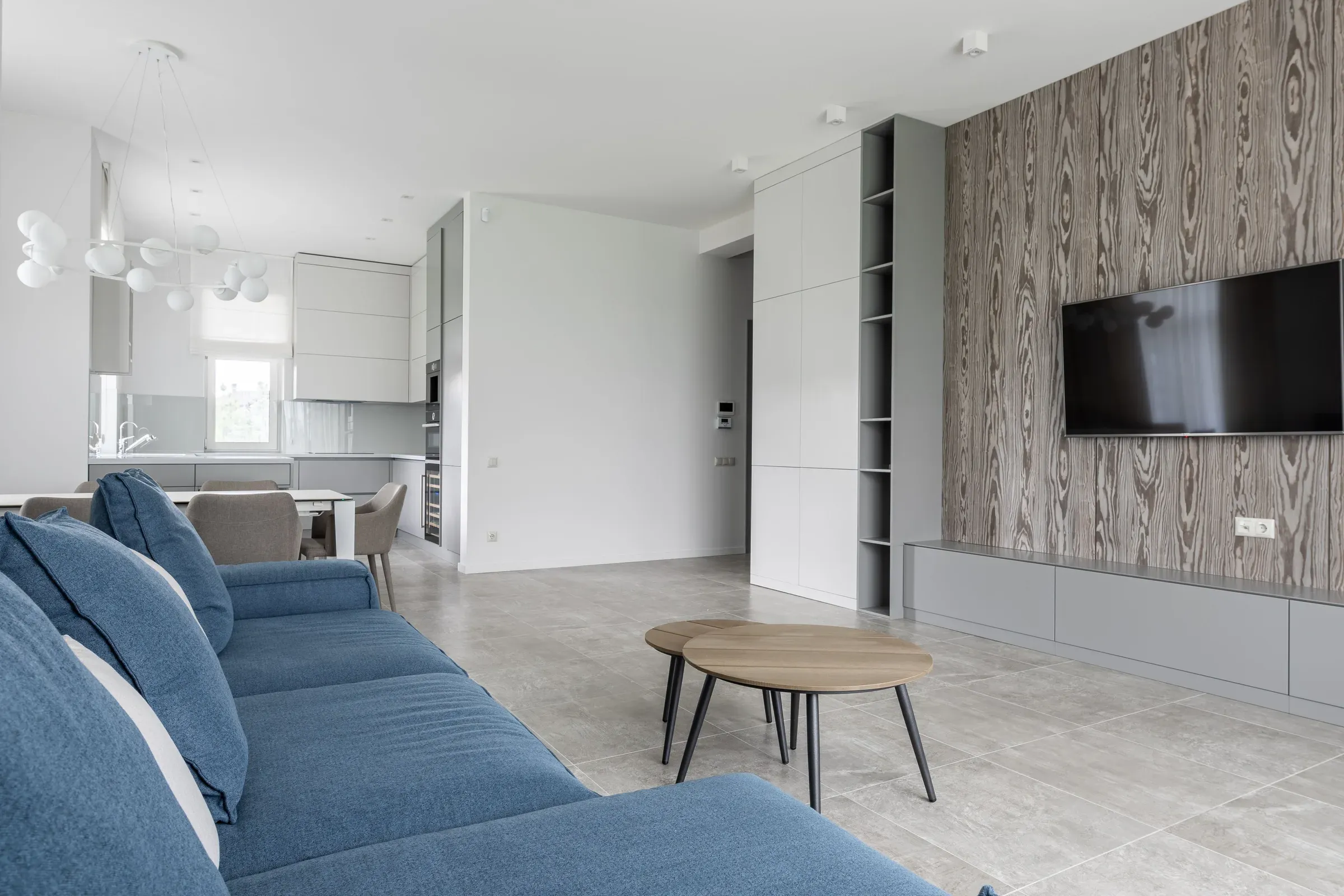 Living room with a blue sofa, wood-grain TV feature wall, grey floating TV unit and nesting tables