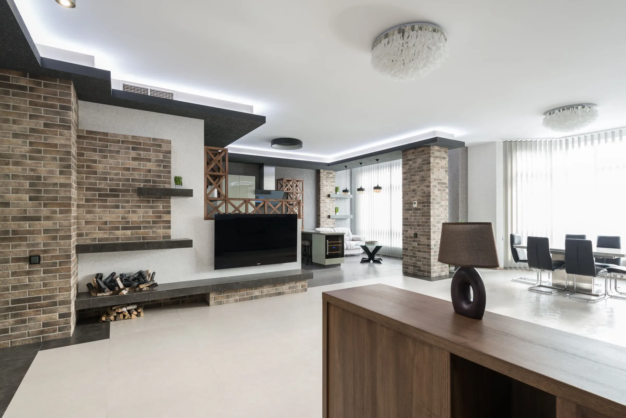 Open-plan living room with a brick-clad TV wall, firewood niche, wooden partition screen and dining area