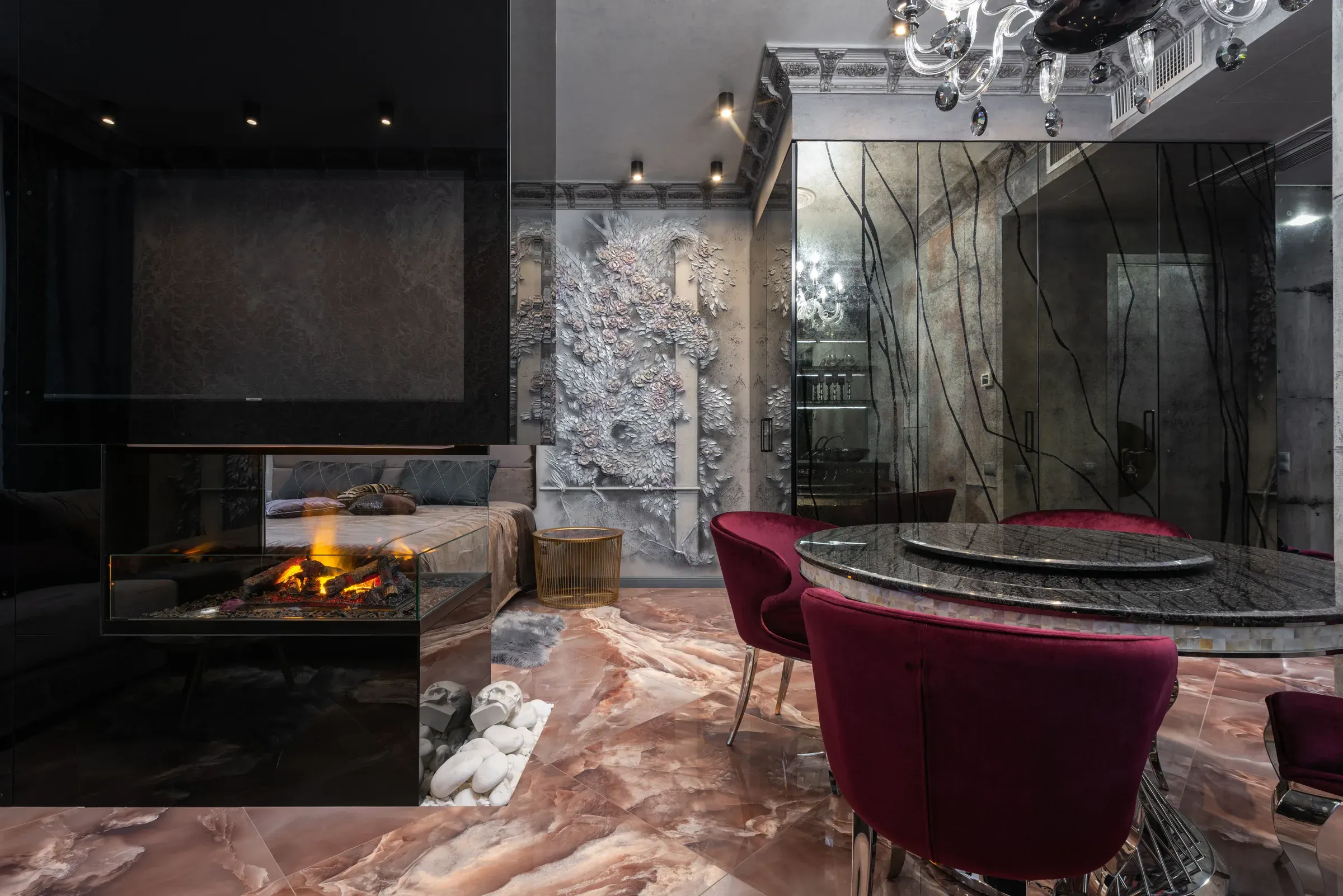Dark luxe room with a glass fireplace, sculpted relief wall, rose marble floor and maroon velvet dining chairs