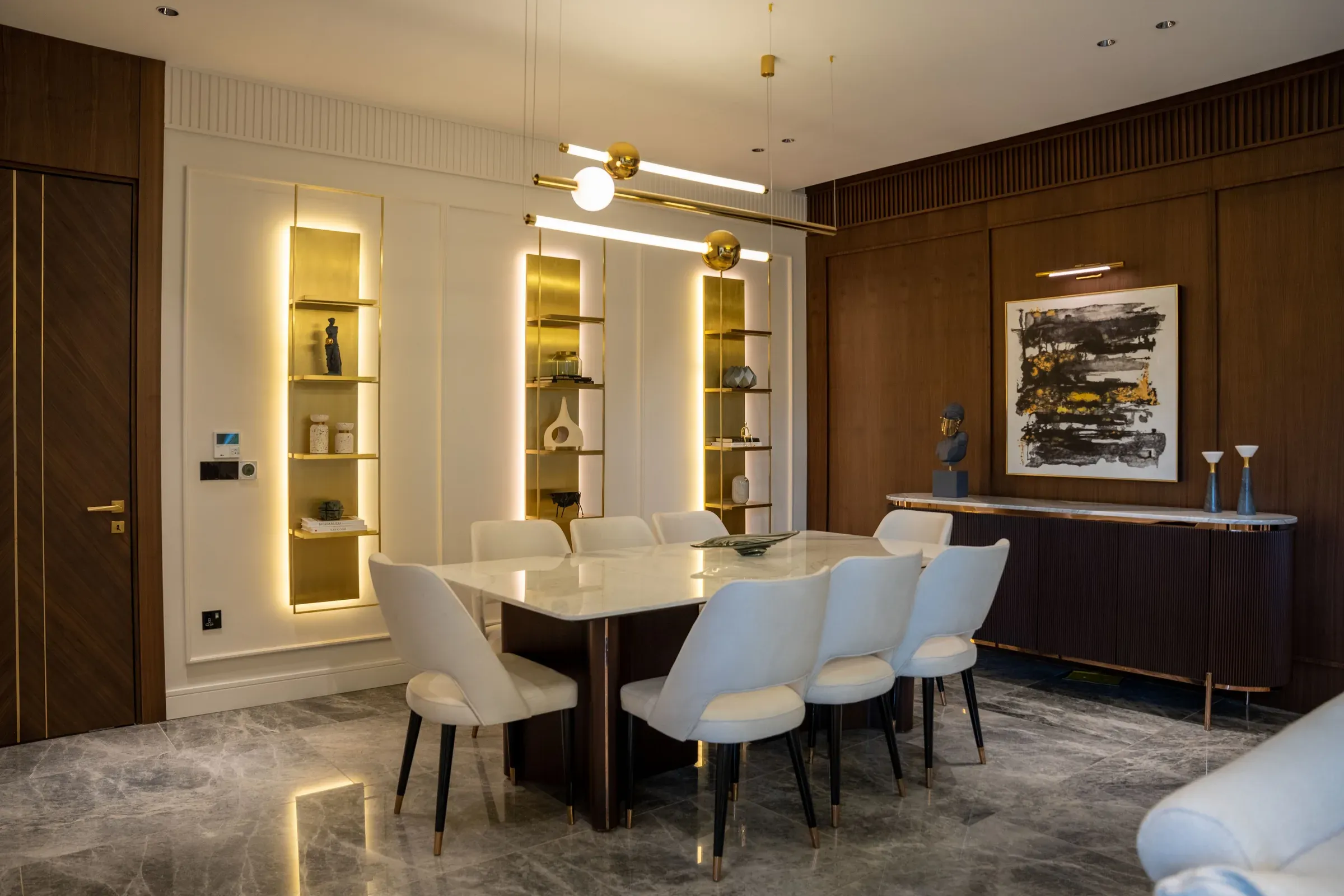 Dining room with backlit gold display niches, a marble-top table, white chairs and walnut wall panels
