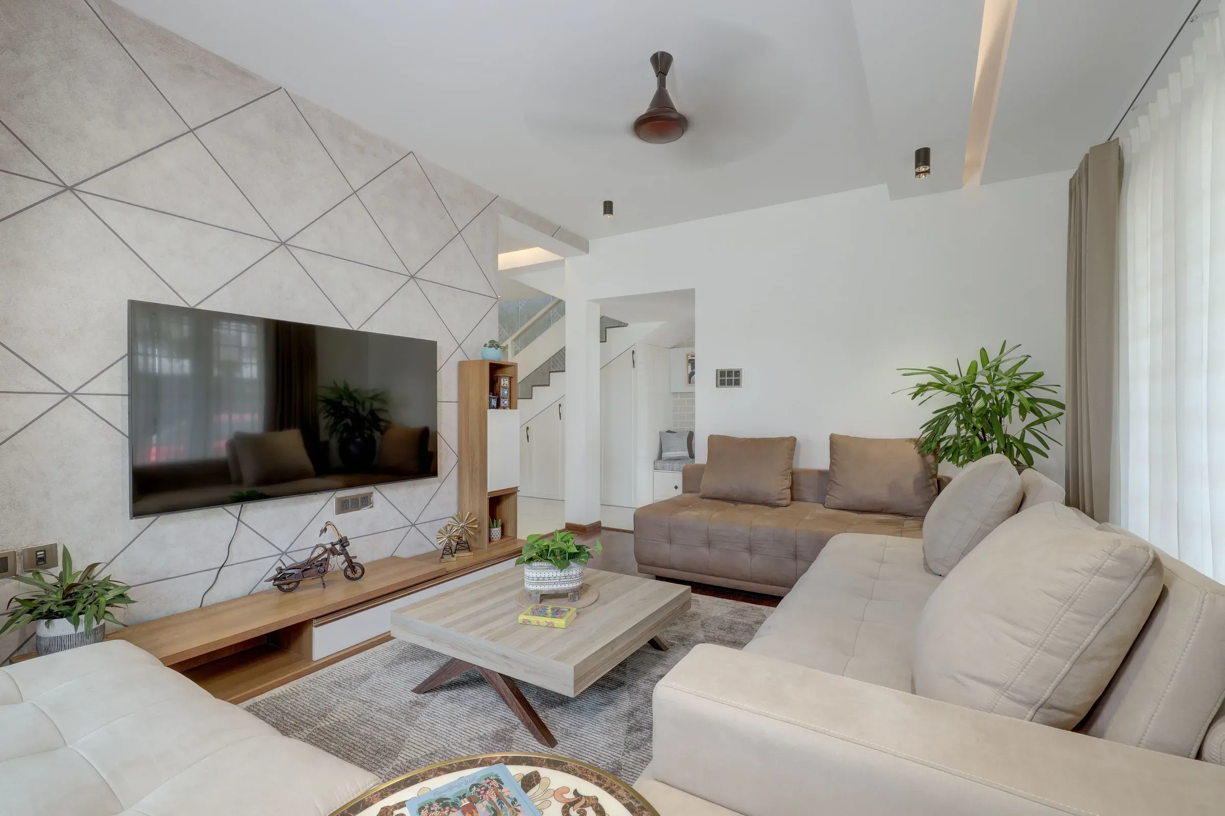 Living room with a geometric-patterned TV wall, wooden TV unit, beige sofas and a staircase behind