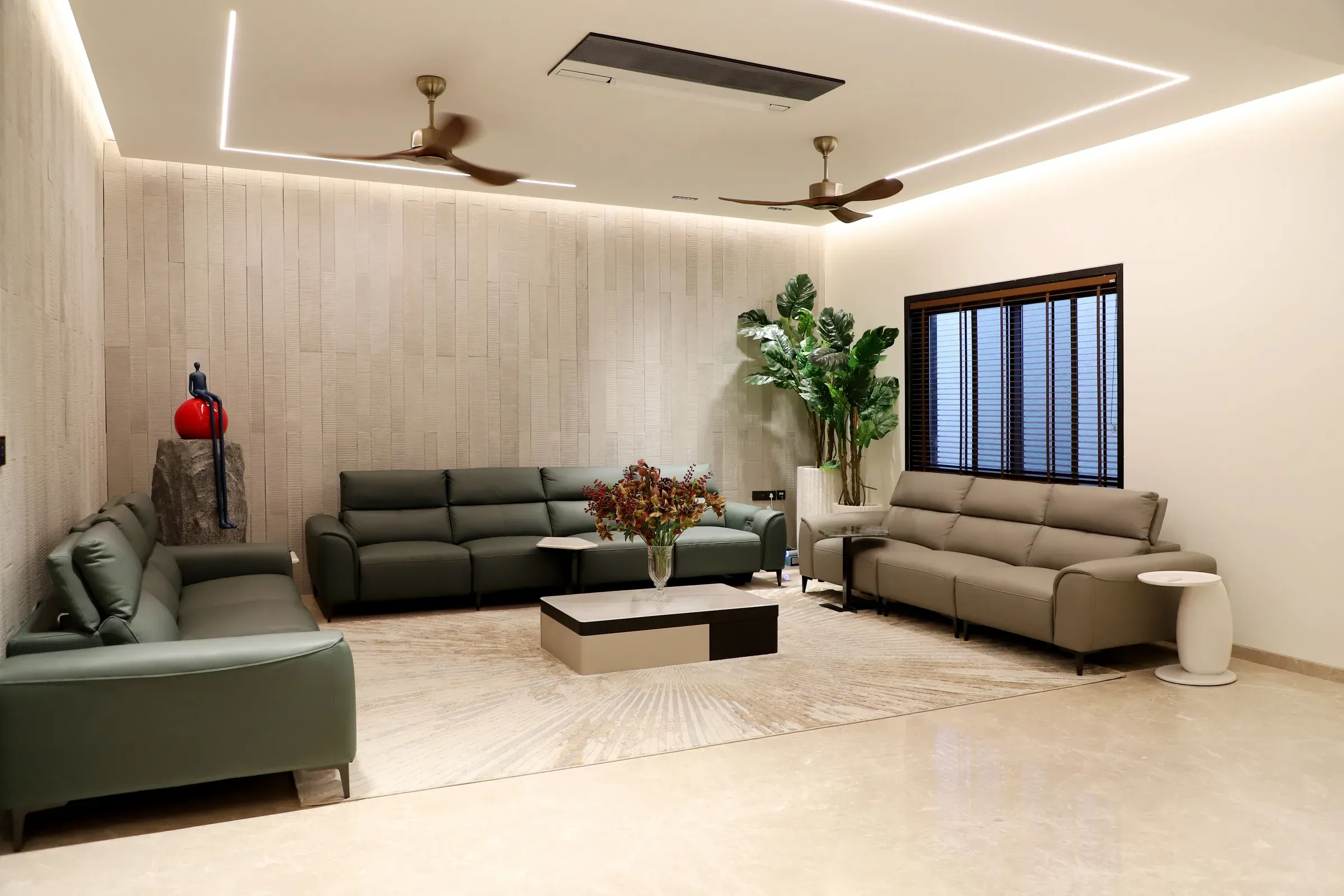 Large Indian living room with green leather sofas, an LED-line ceiling, ceiling fans and a textured stone wall