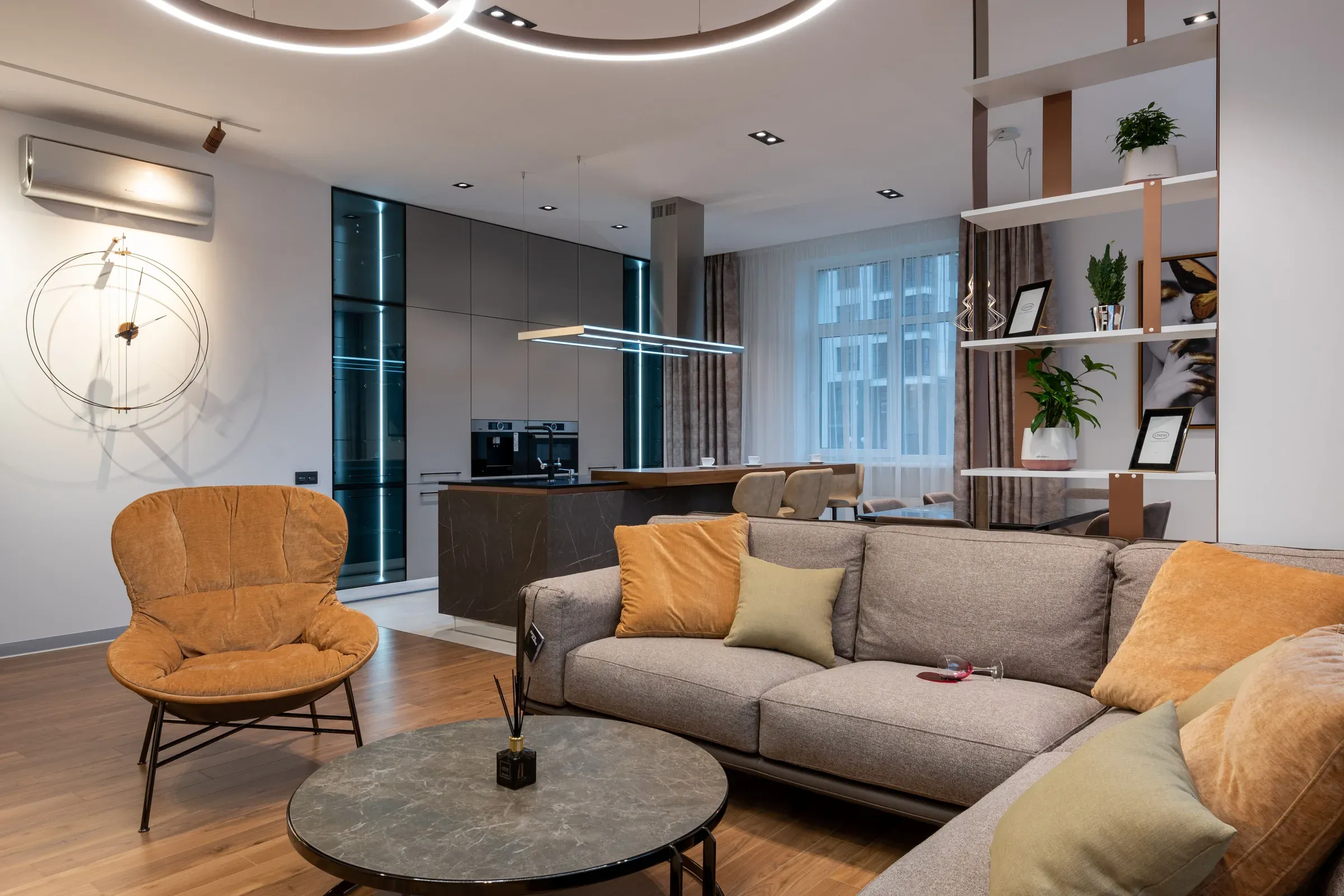 Living room with a grey sectional sofa, mustard cushions, orange armchair, open kitchen and shelf partition