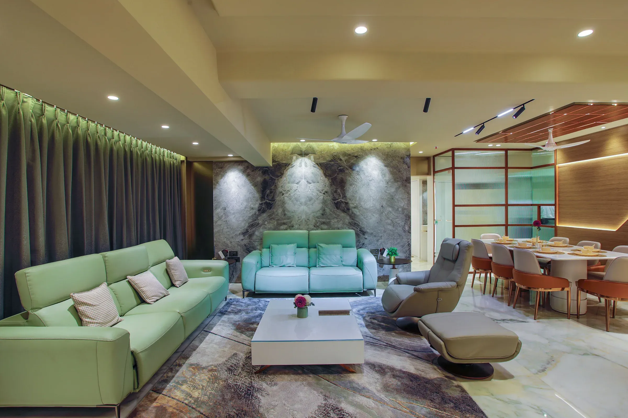 Long Indian living room with mint leather sofas, stone feature wall, recliner and dining area with ceiling fans
