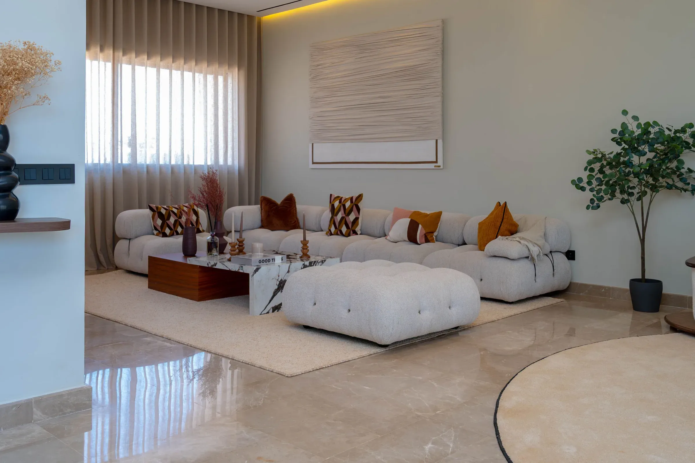 Bright living room with a modular boucle sofa, tufted ottoman, marble floor and woven wall art