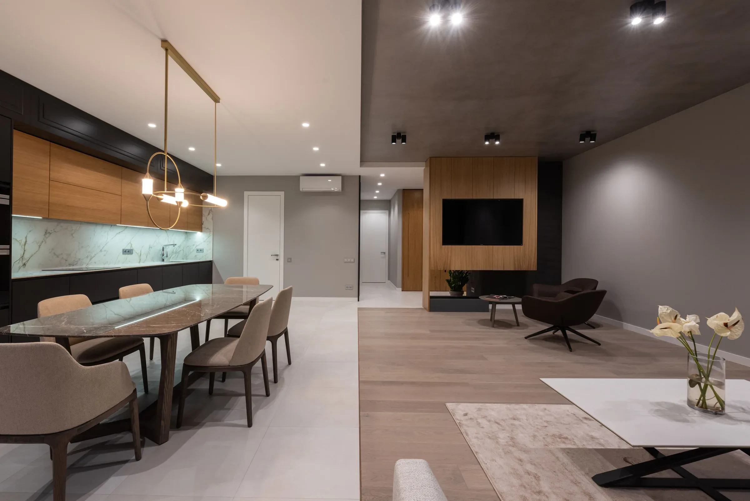 Open-plan living, dining and kitchen with a wooden TV wall, marble dining table and brass ring pendant