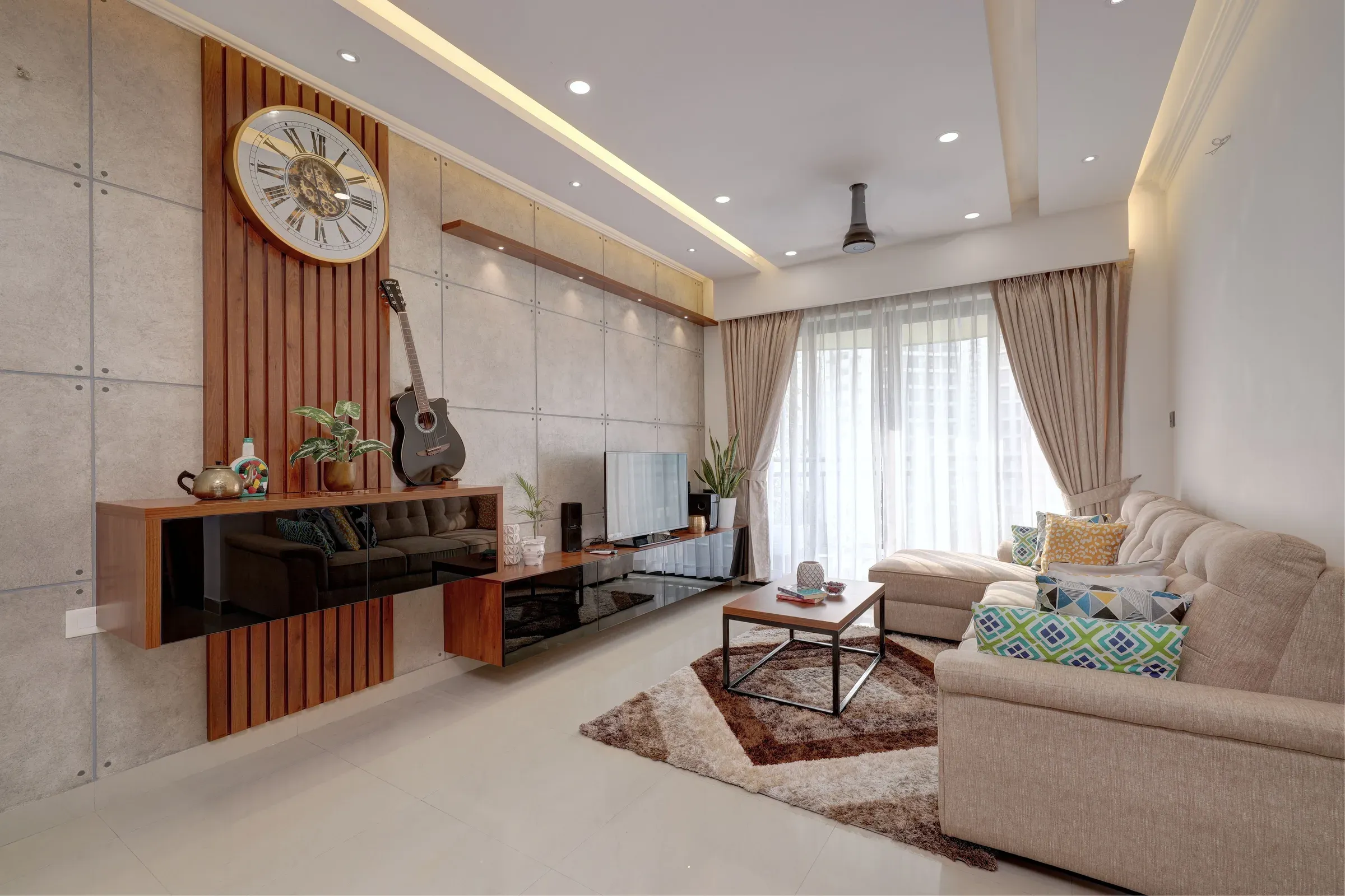 Indian flat living room with a slatted wood console wall, large wall clock, concrete-look tiles and beige sofa set