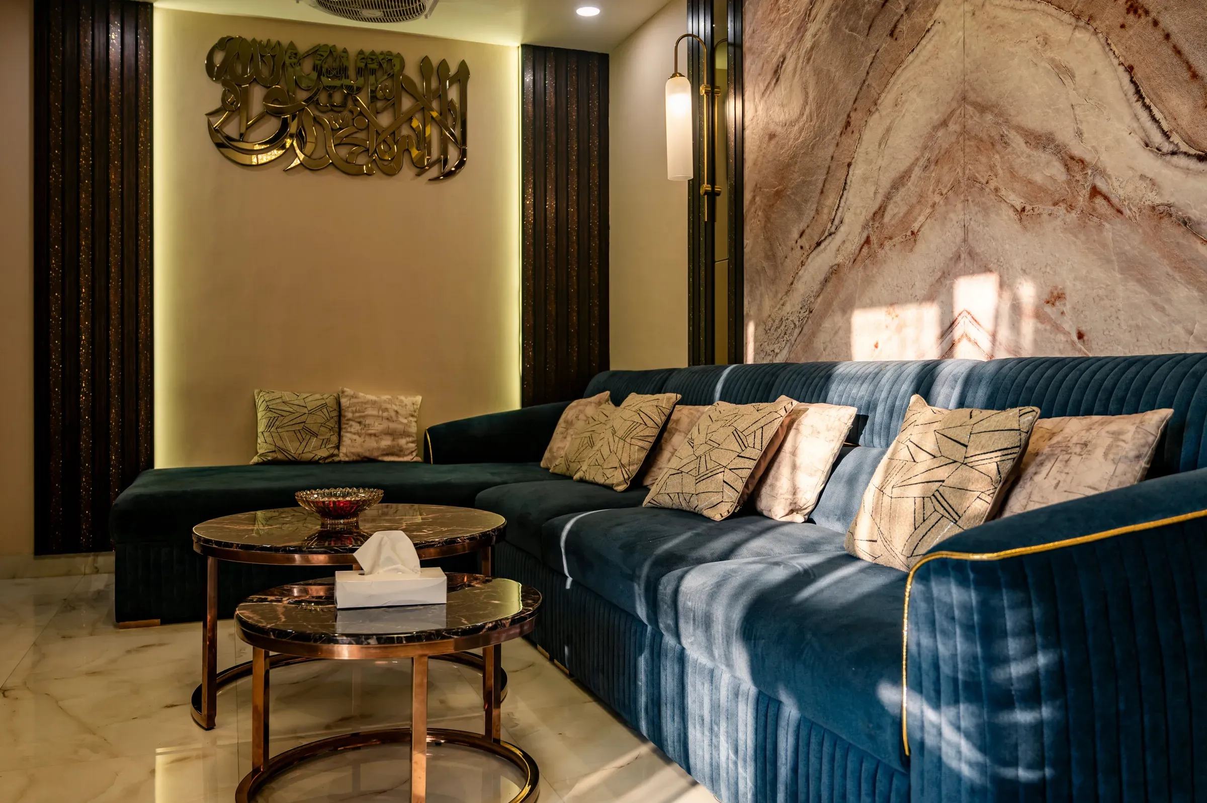 Living room with a teal channel-tufted velvet sofa, gold calligraphy wall art, marble wall and nesting tables