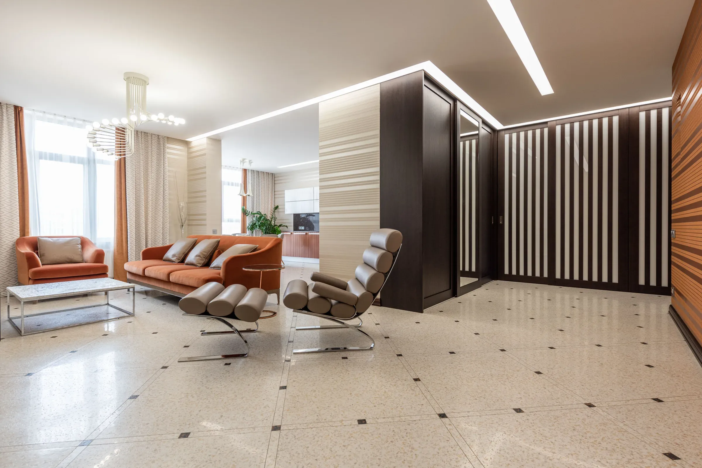 Living room with a terrazzo floor, rust sofa and armchair, chrome lounger and striped wall panels