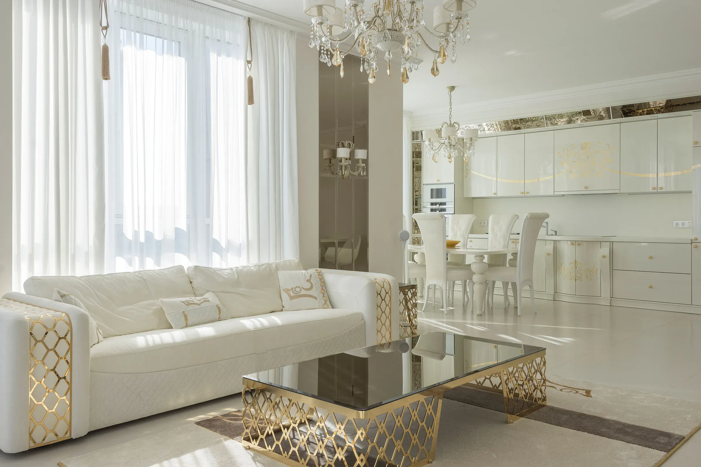 Bright white living room with a gold-trim sofa, gold coffee table, crystal chandeliers and dining area