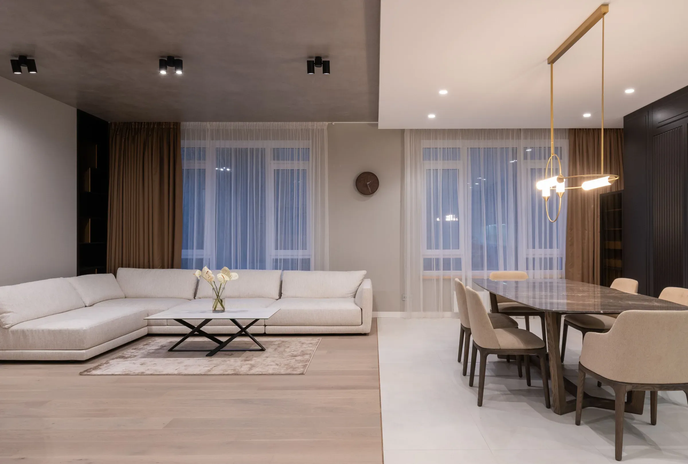 Calm living room with a white sectional sofa, marble dining table, brass pendant and sheer curtains