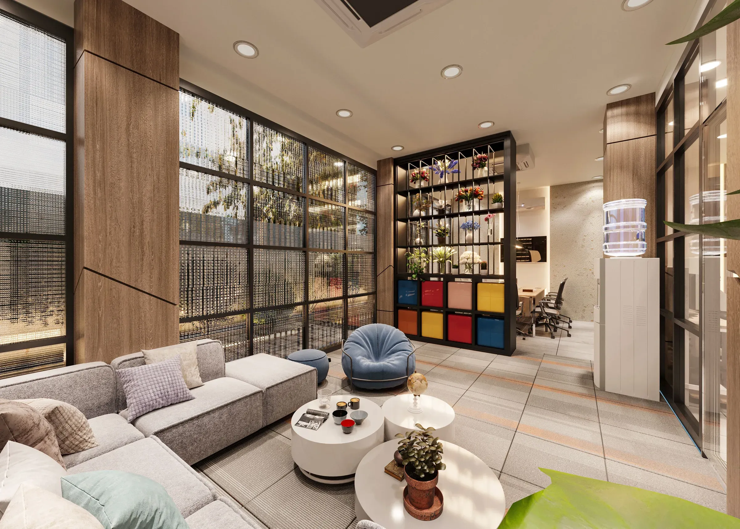 Office lounge with a grey sofa, round tables, glass wall, colourful cubby shelf and work area behind