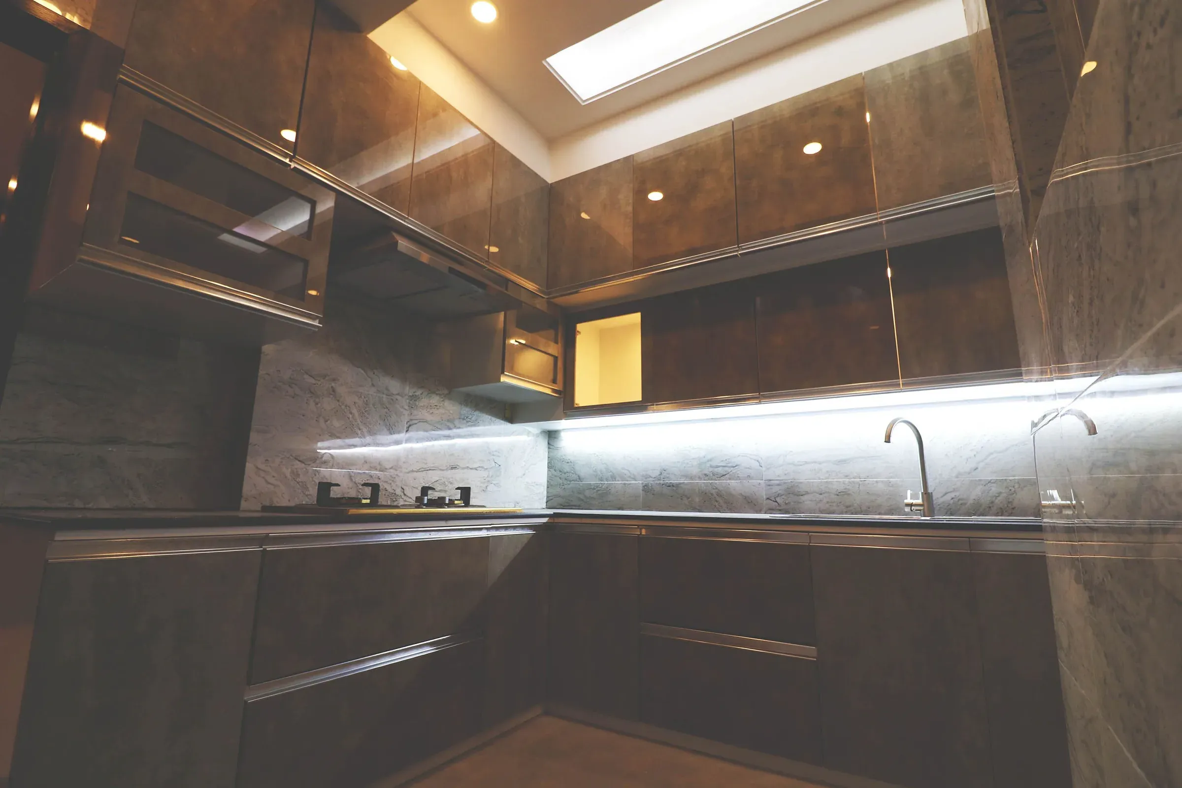 Dark gloss kitchen with a skylight, grey stone backsplash and under-cabinet LED strip lighting