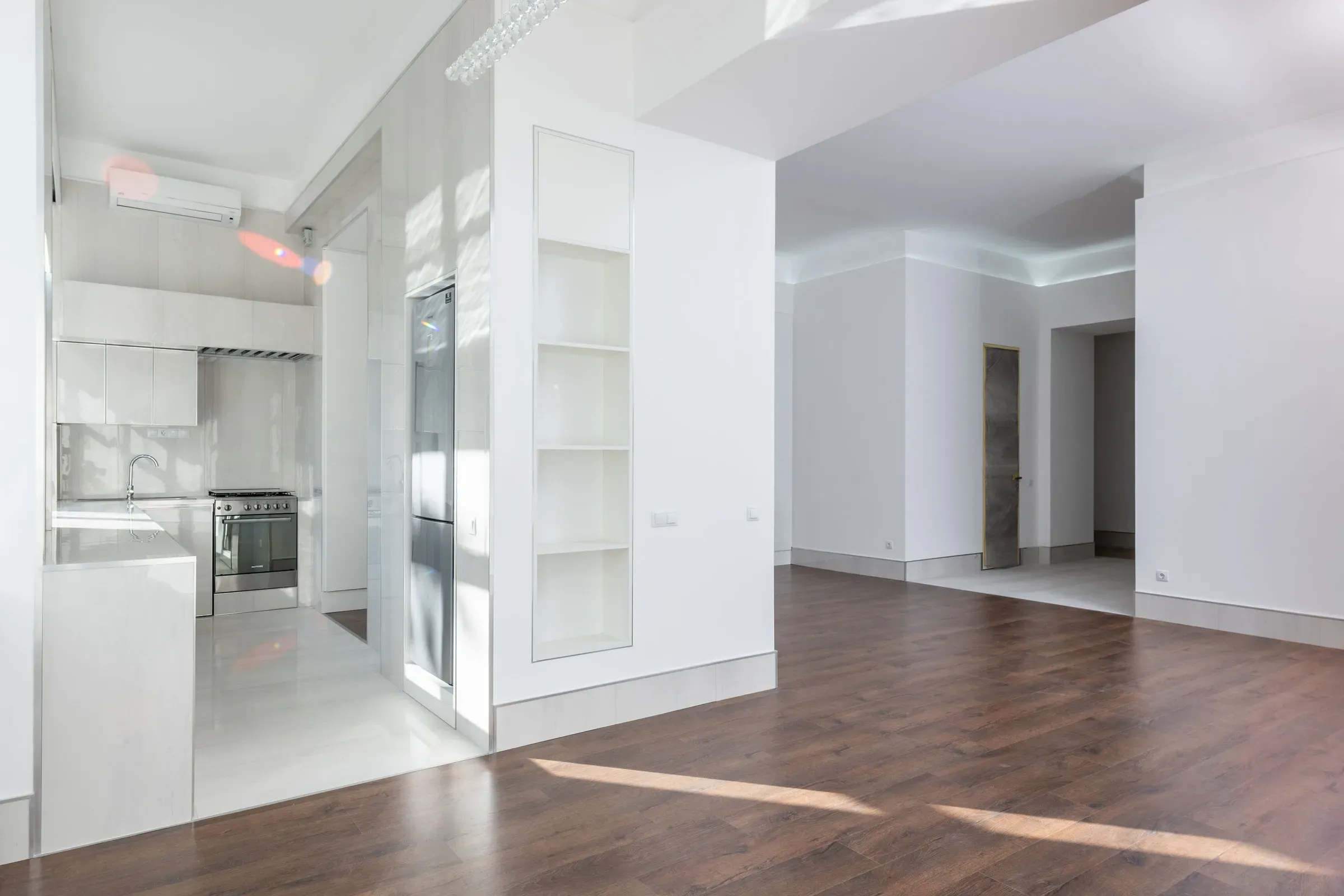 Freshly renovated empty flat with white walls, built-in niche shelves, laminate wood floor and a white kitchen