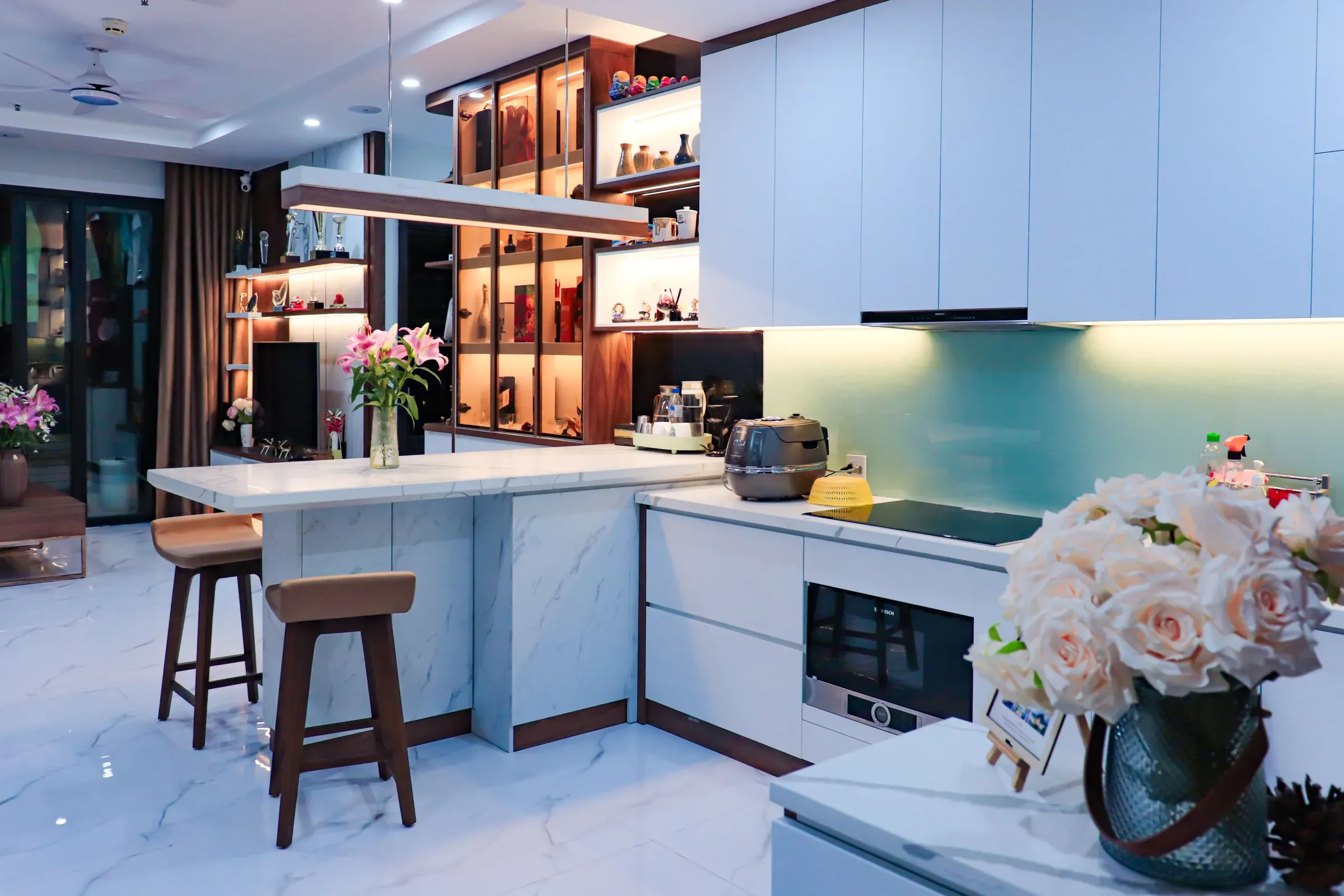 Renovated white kitchen with a marble breakfast island, bar stools, aqua backsplash and lit display shelves