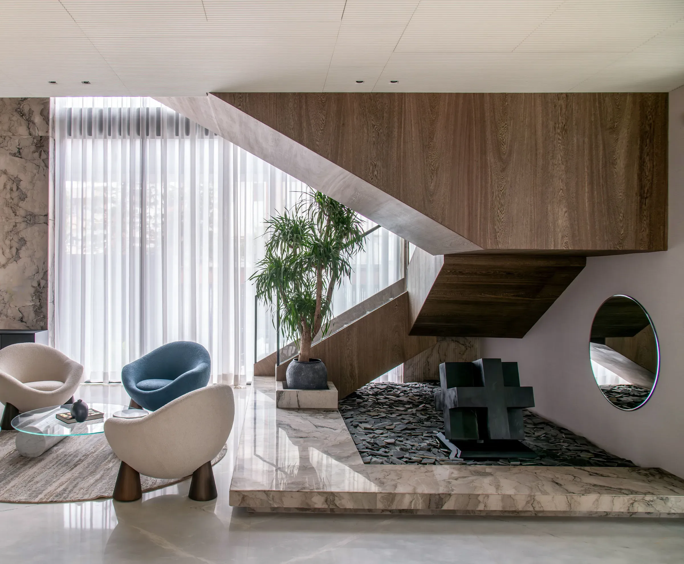 Luxury living room with a floating wooden staircase over a pebble bed, boucle armchairs and a round mirror