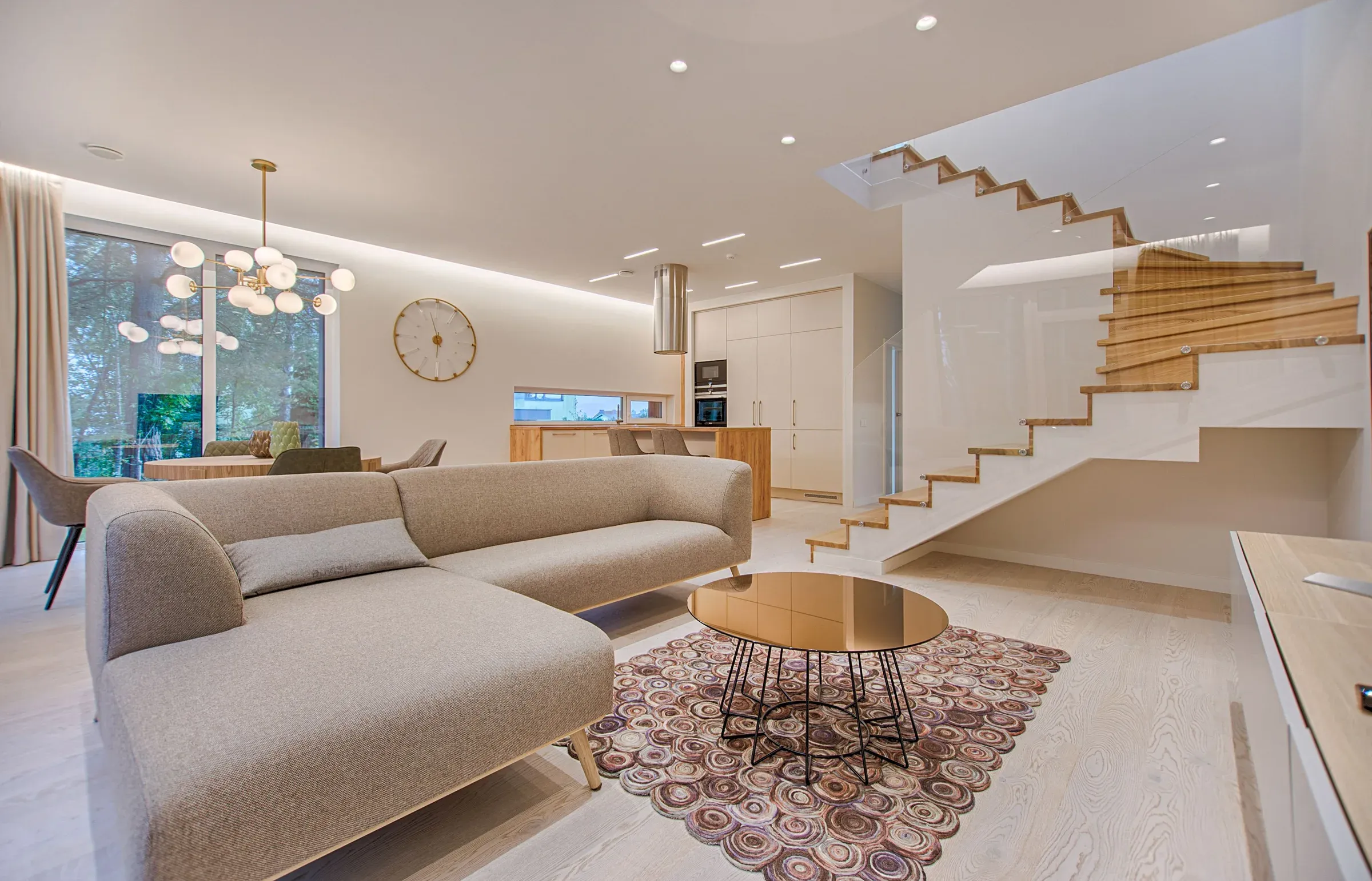 Bright white living room with a floating oak staircase, grey sectional, globe chandelier and wood-slice rug