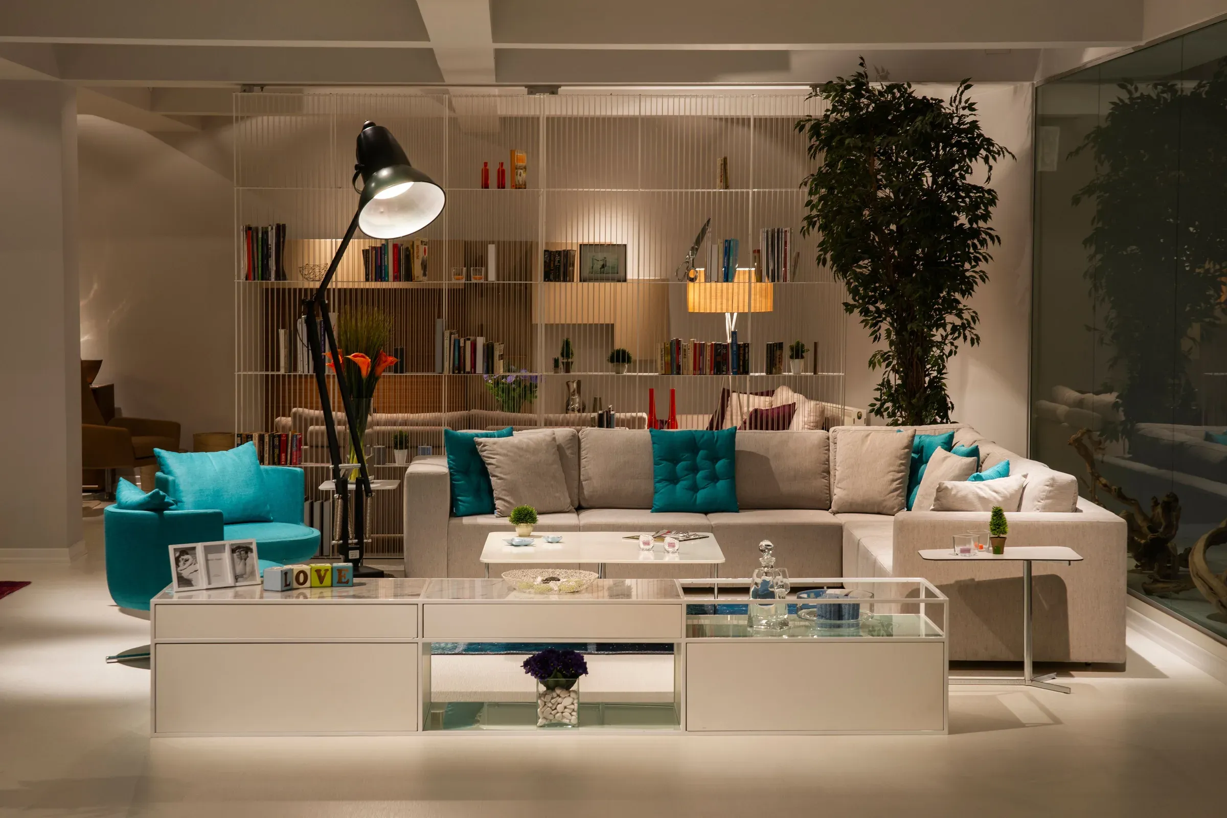 Bright room with a full-height white bookshelf partition, white sectional, turquoise chair and arc floor lamp