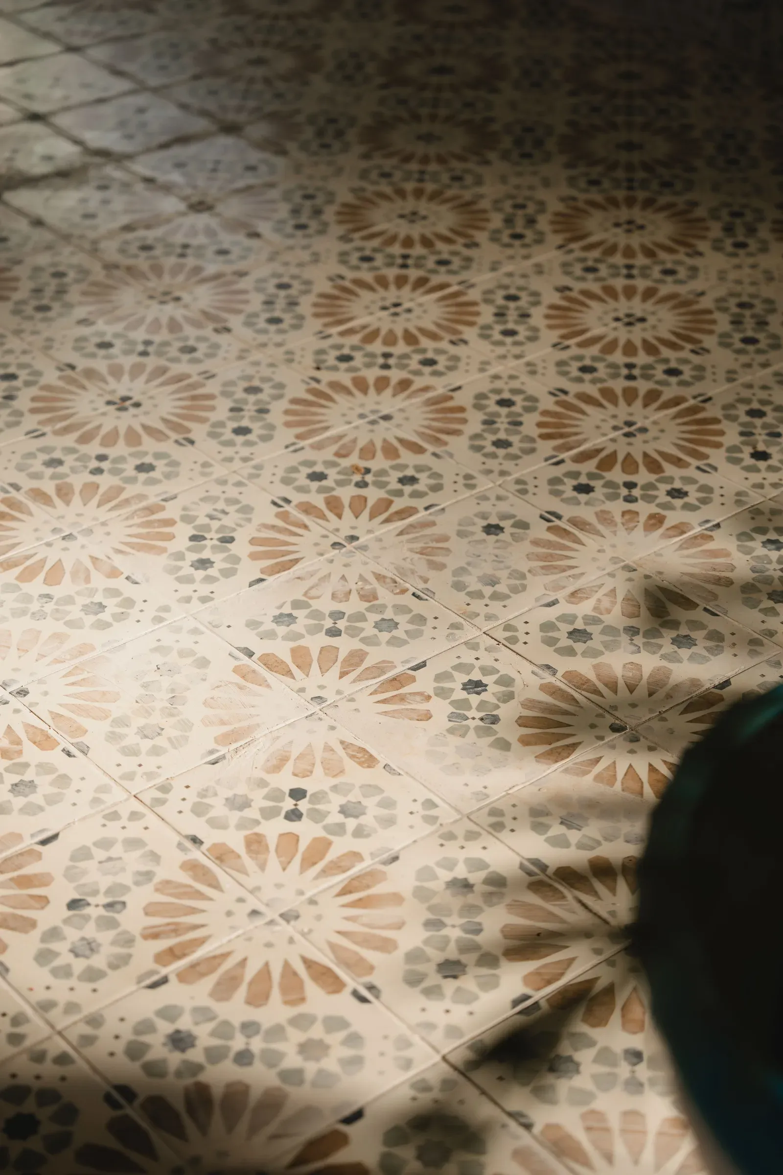Moroccan-style patterned floor tiles in terracotta and grey with dappled sunlight
