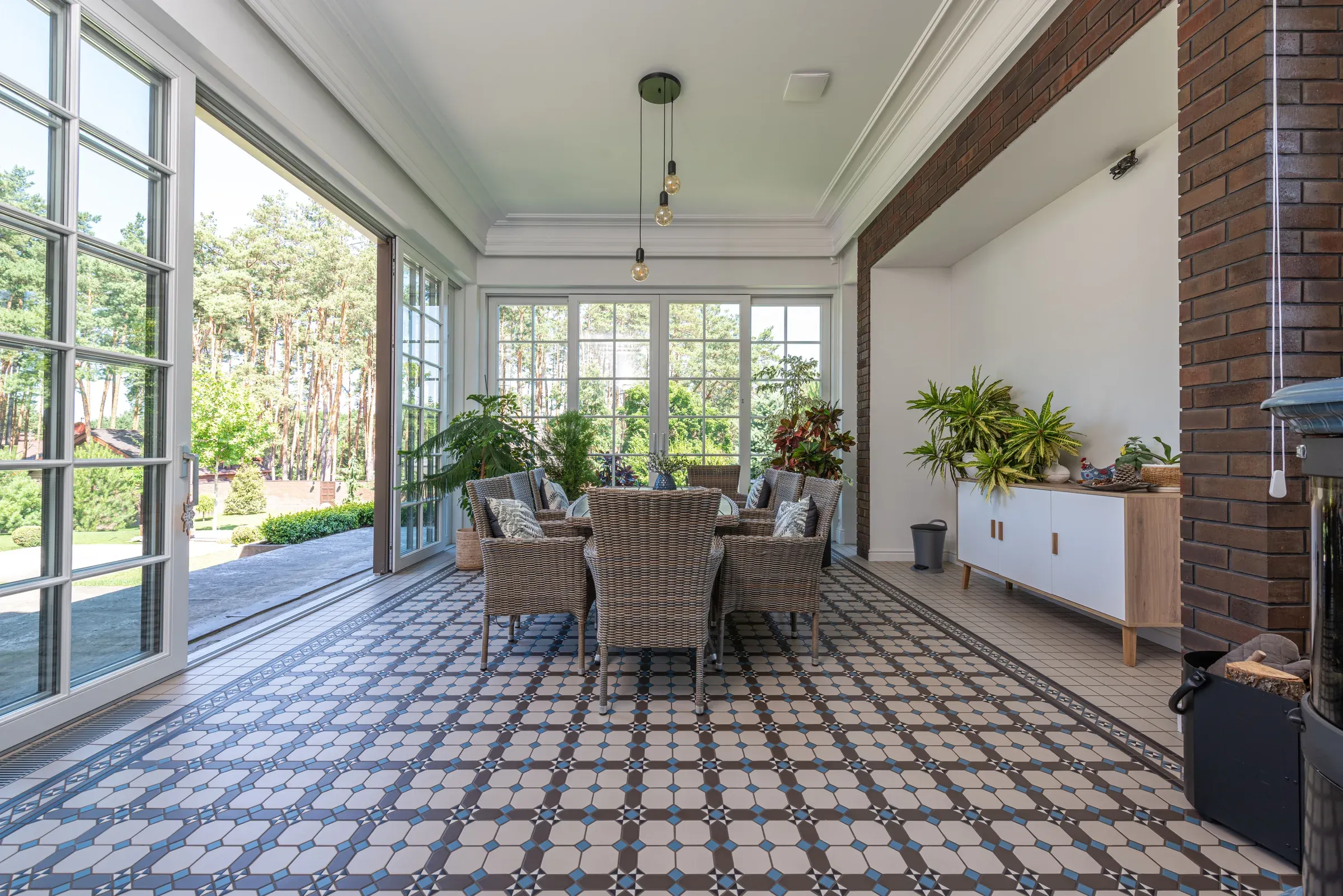 Bright sunroom with a patterned encaustic-style tile floor, wicker dining set and garden views