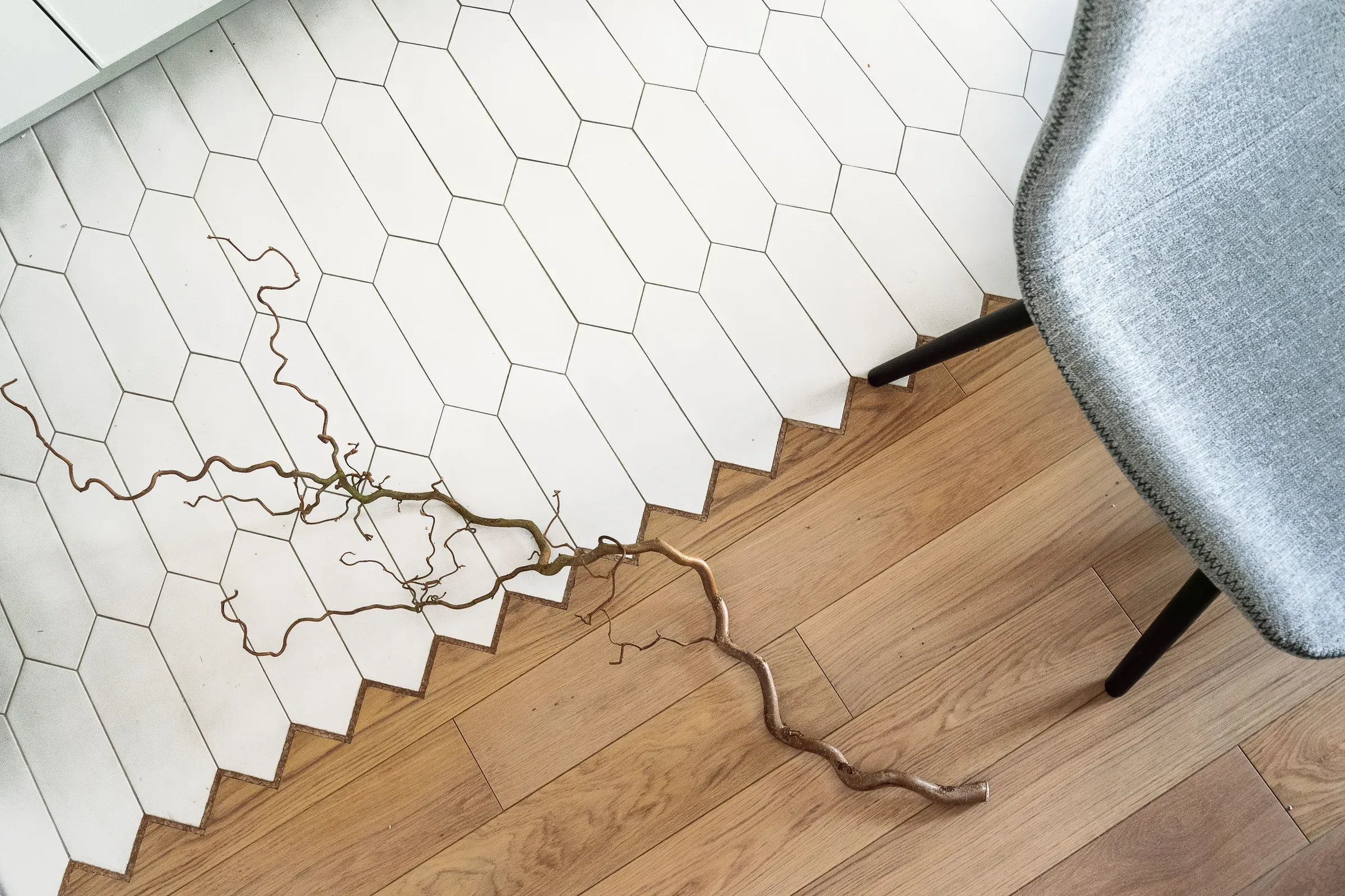 White elongated hexagon tiles meeting an oak wooden floor in a zigzag transition