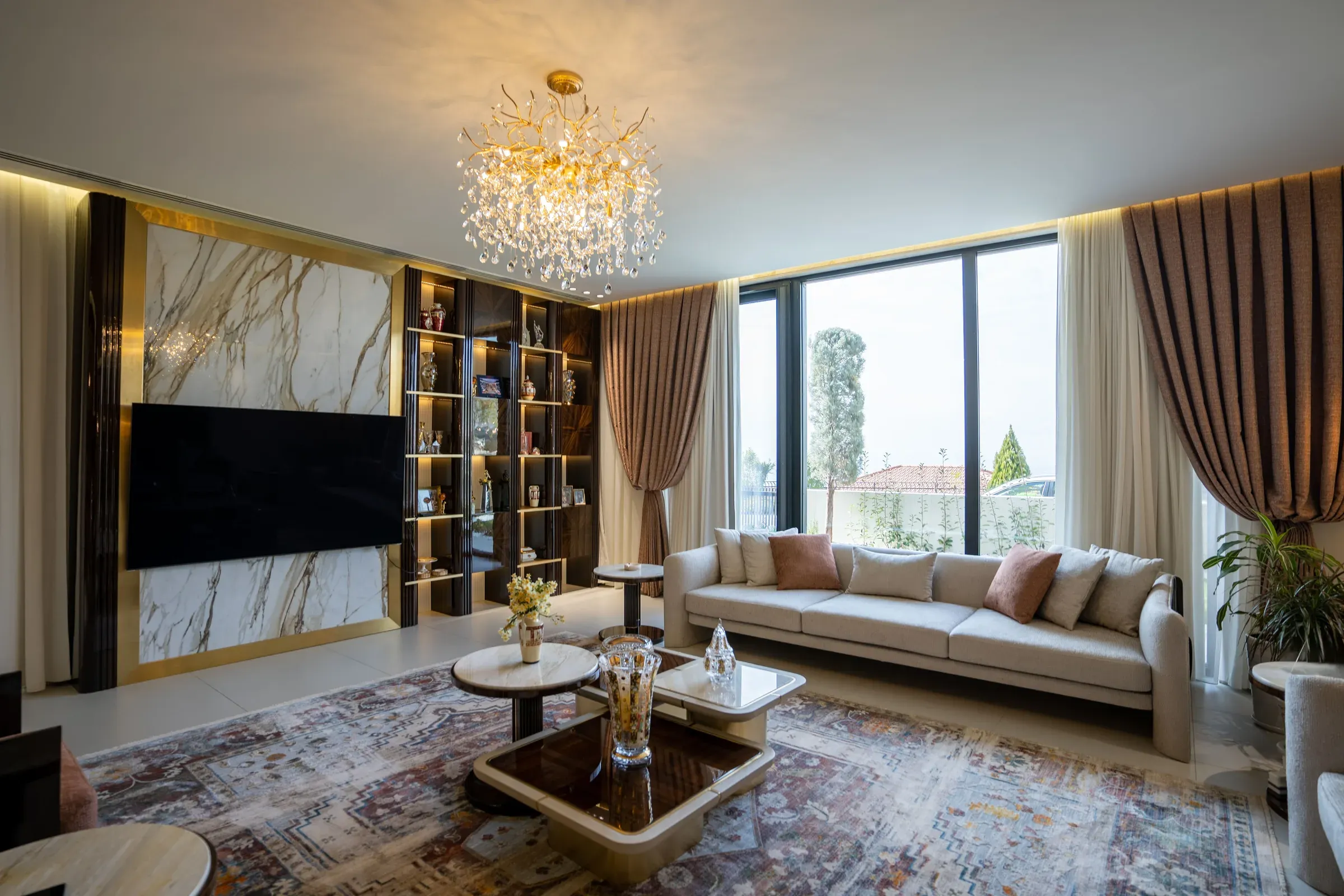 Luxury living room with a TV on a marble panel framed in gold, lit display shelves and a crystal chandelier