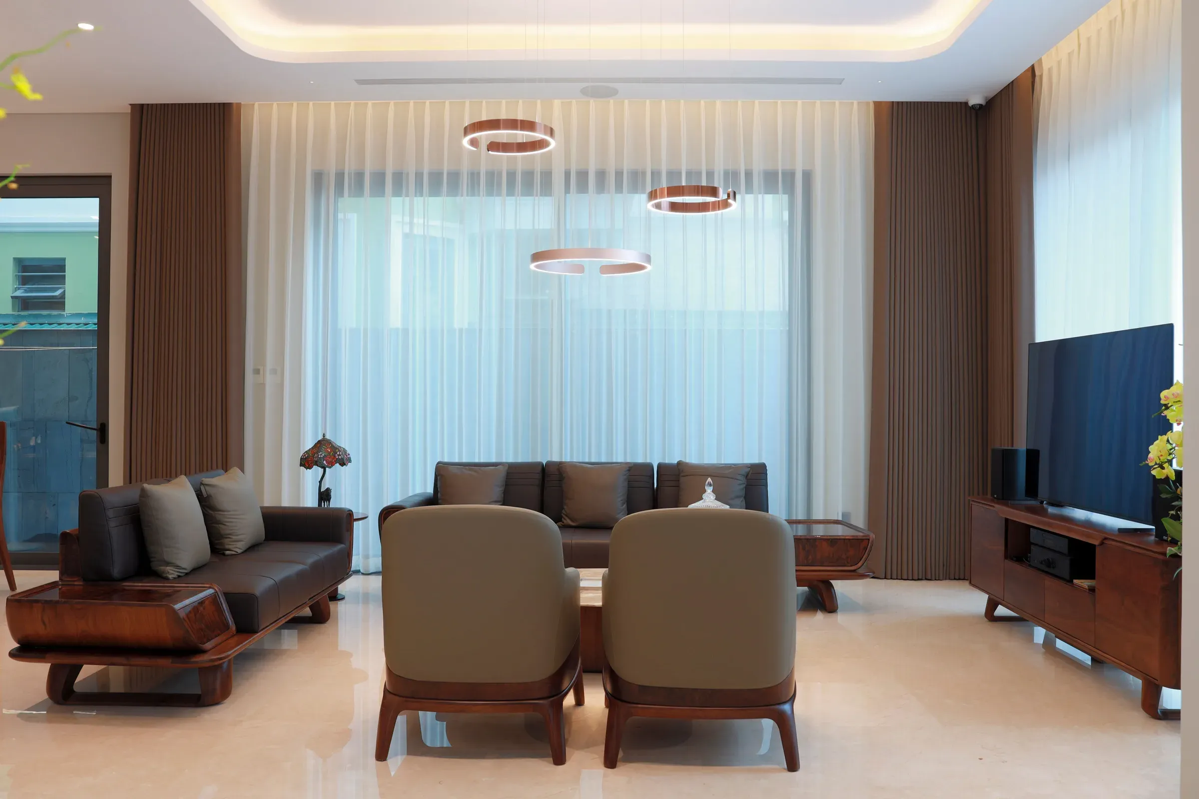 Living room with a standing walnut TV unit, walnut-framed sofas, ring pendant lights and sheer curtains