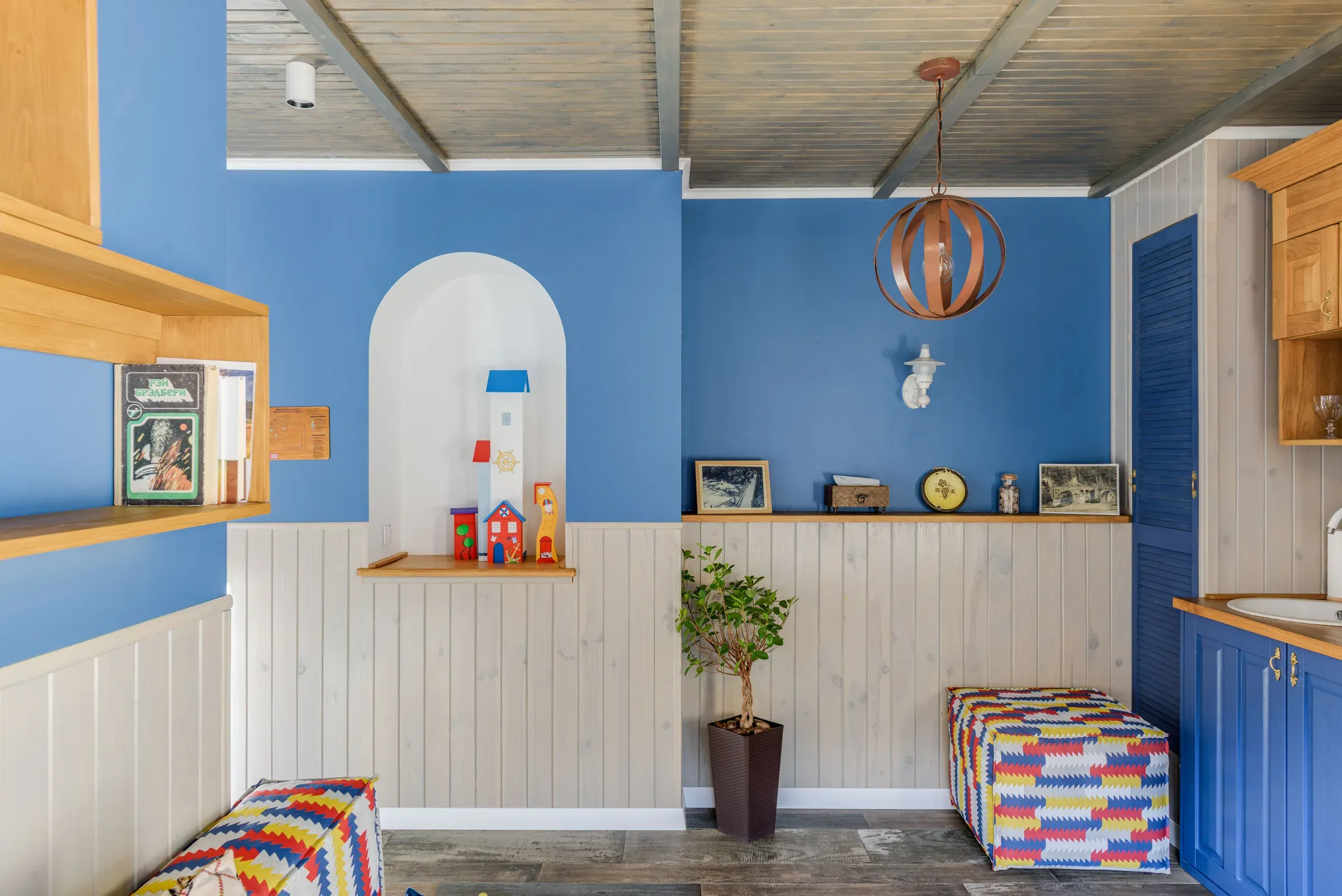 Bright room with blue walls above white wooden dado panelling, an arched niche with toy houses and wall shelf