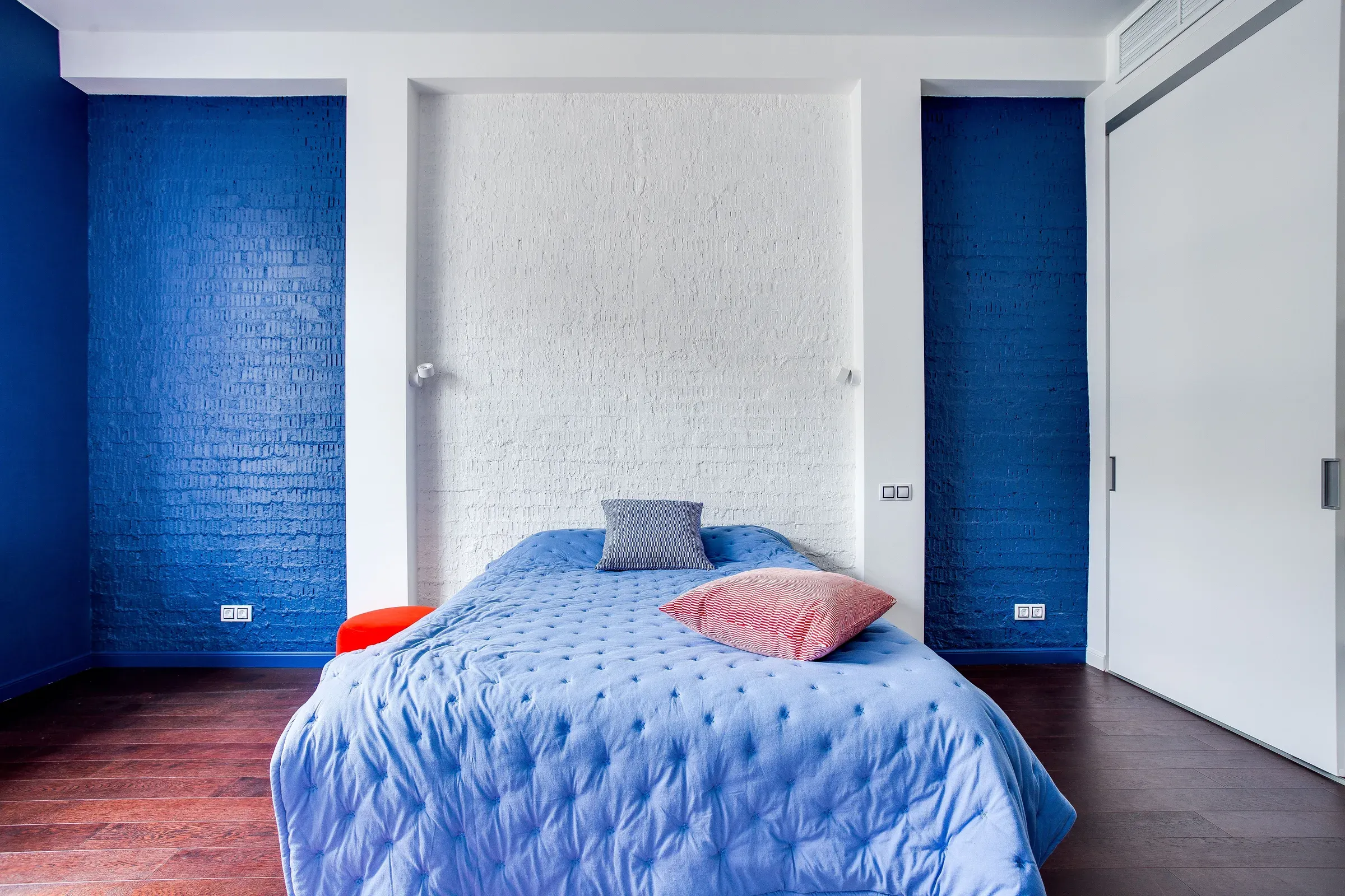 Bedroom with cobalt blue painted brick walls, a white brick headboard niche and blue quilted bedspread