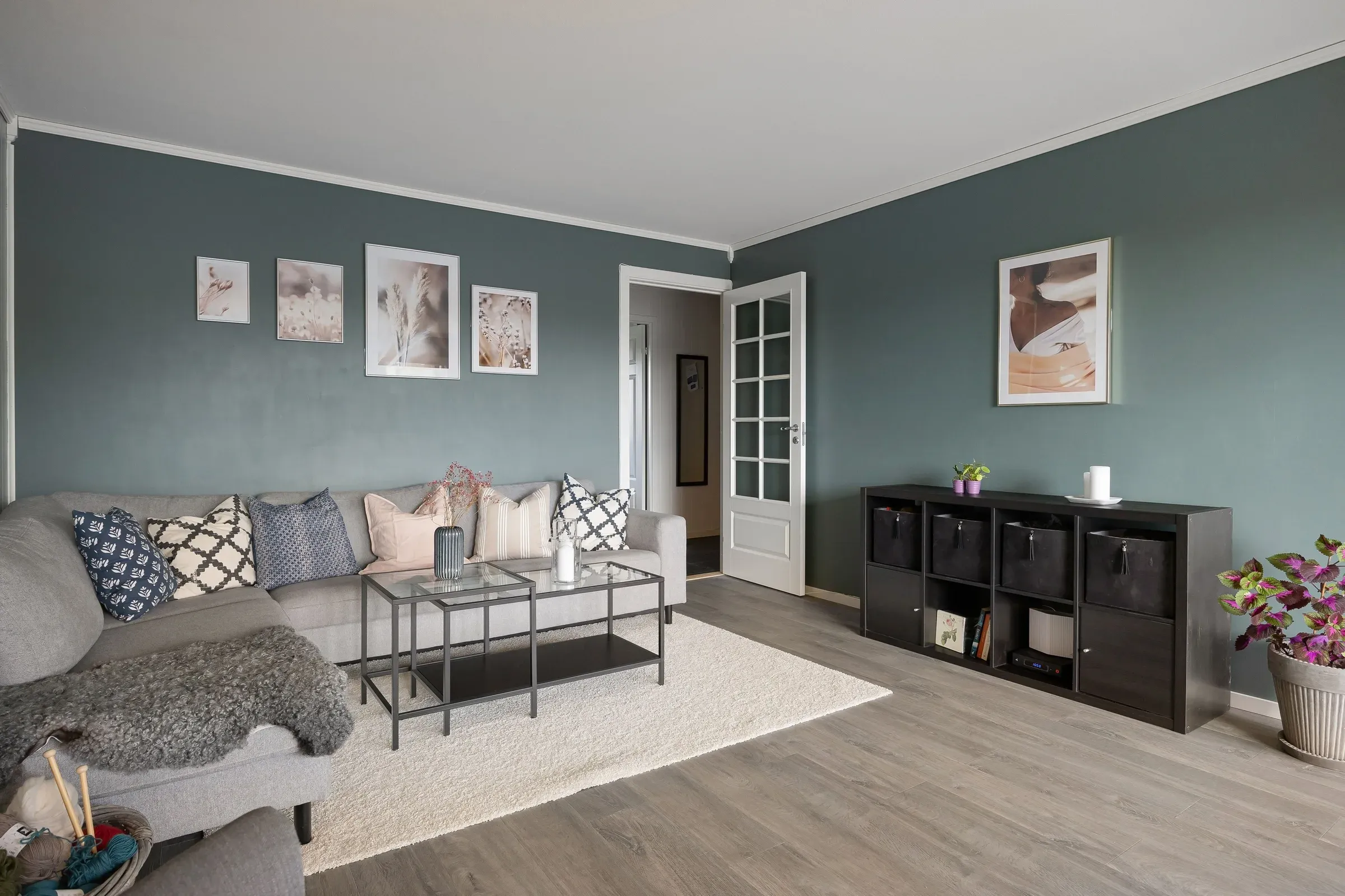 Living room with grey-green walls, white cornice, a grey sofa, framed prints and cube storage unit