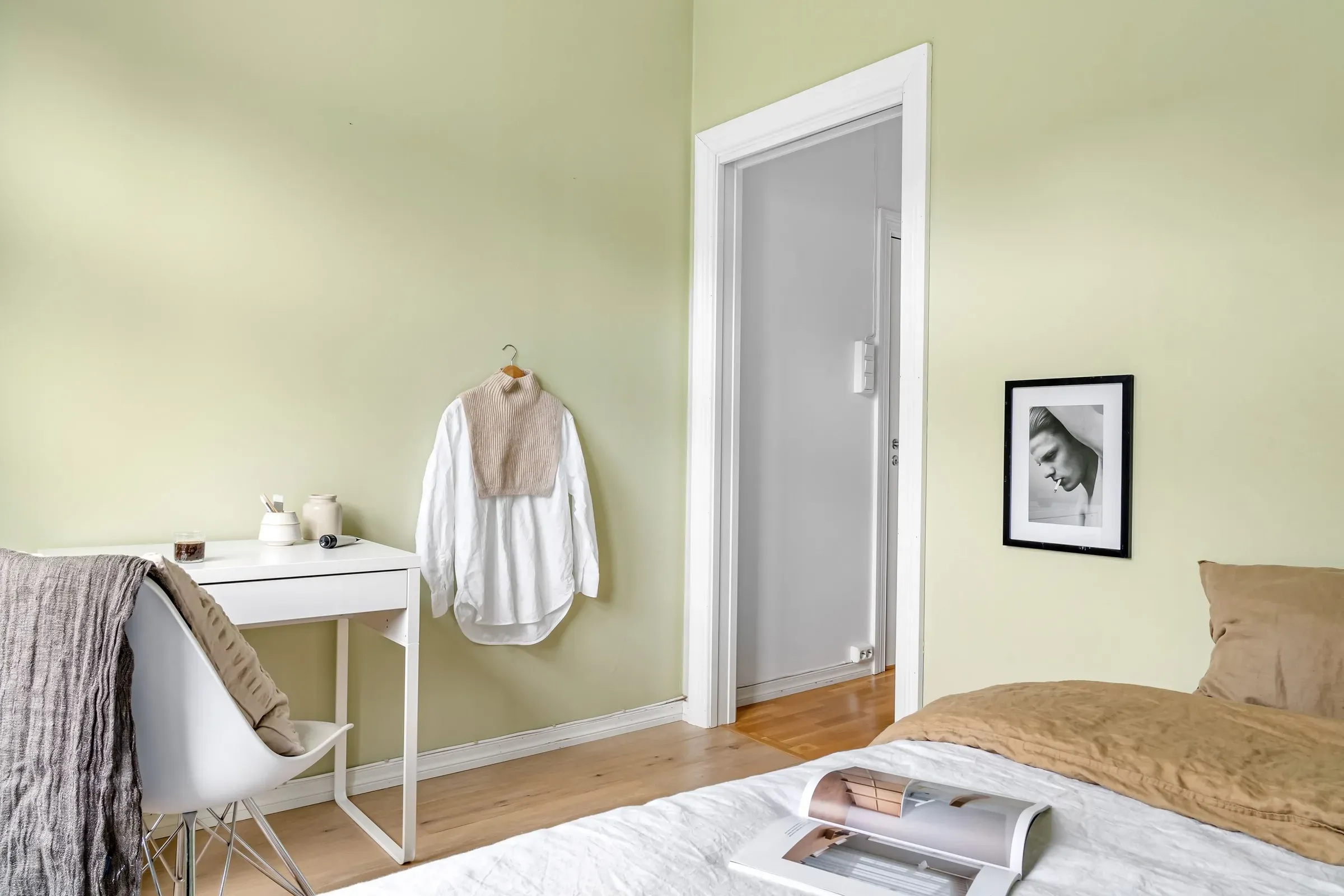 Bedroom with soft pista green walls, white trim, a small white desk and framed portrait