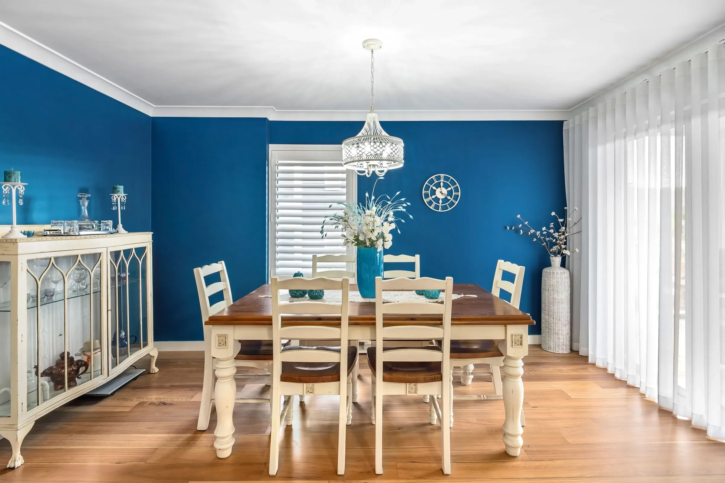 Dining room with royal blue walls, white trim, a cream dining set, chandelier and glass display cabinet