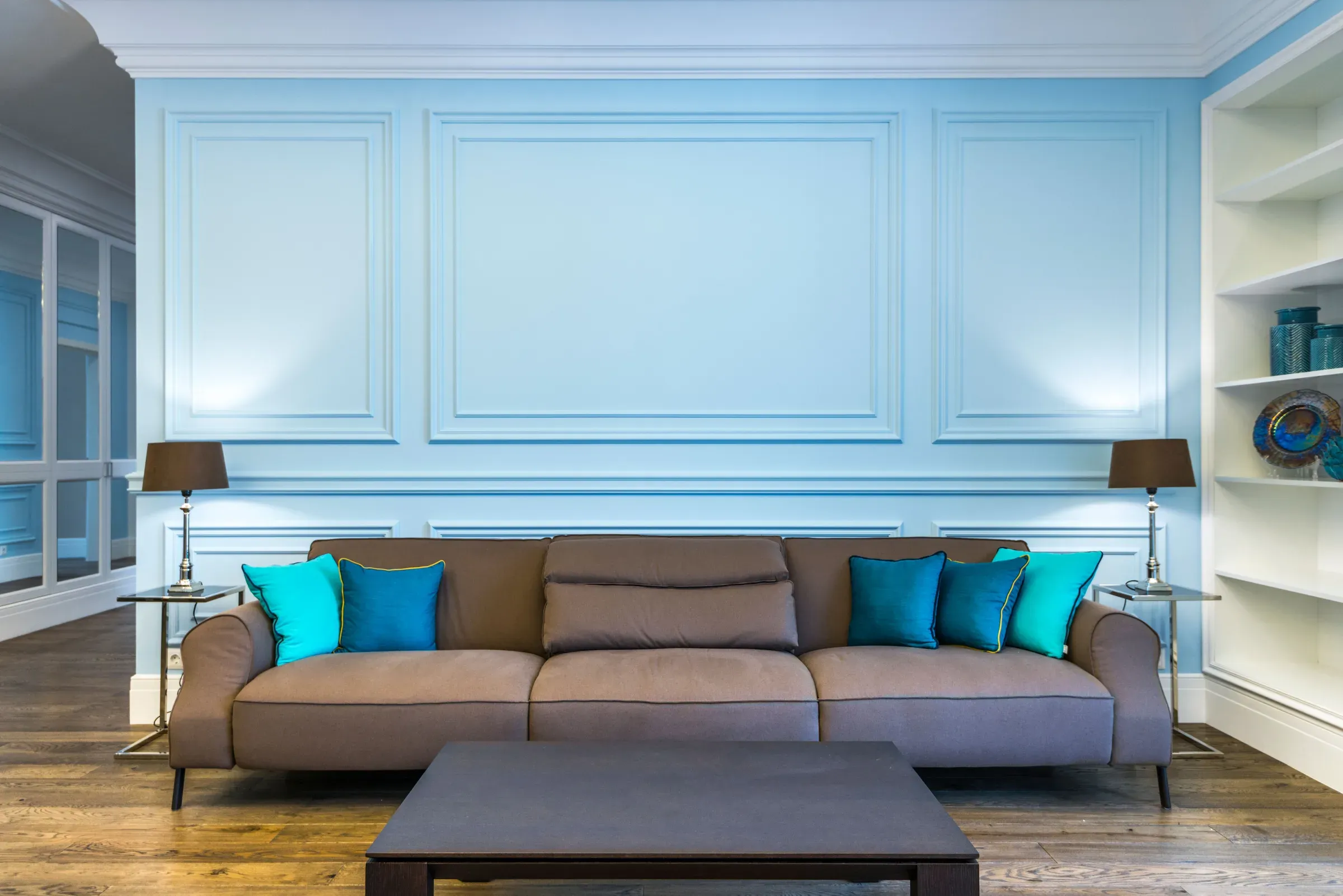 Living room with a sky blue moulded panel wall, brown sofa with turquoise cushions and built-in shelves