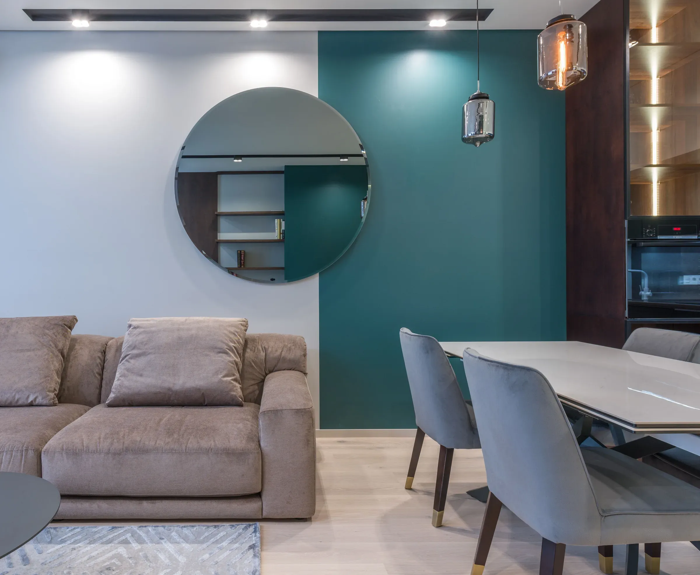 Living-dining room with a teal accent wall, light grey walls, round mirror and grey dining chairs