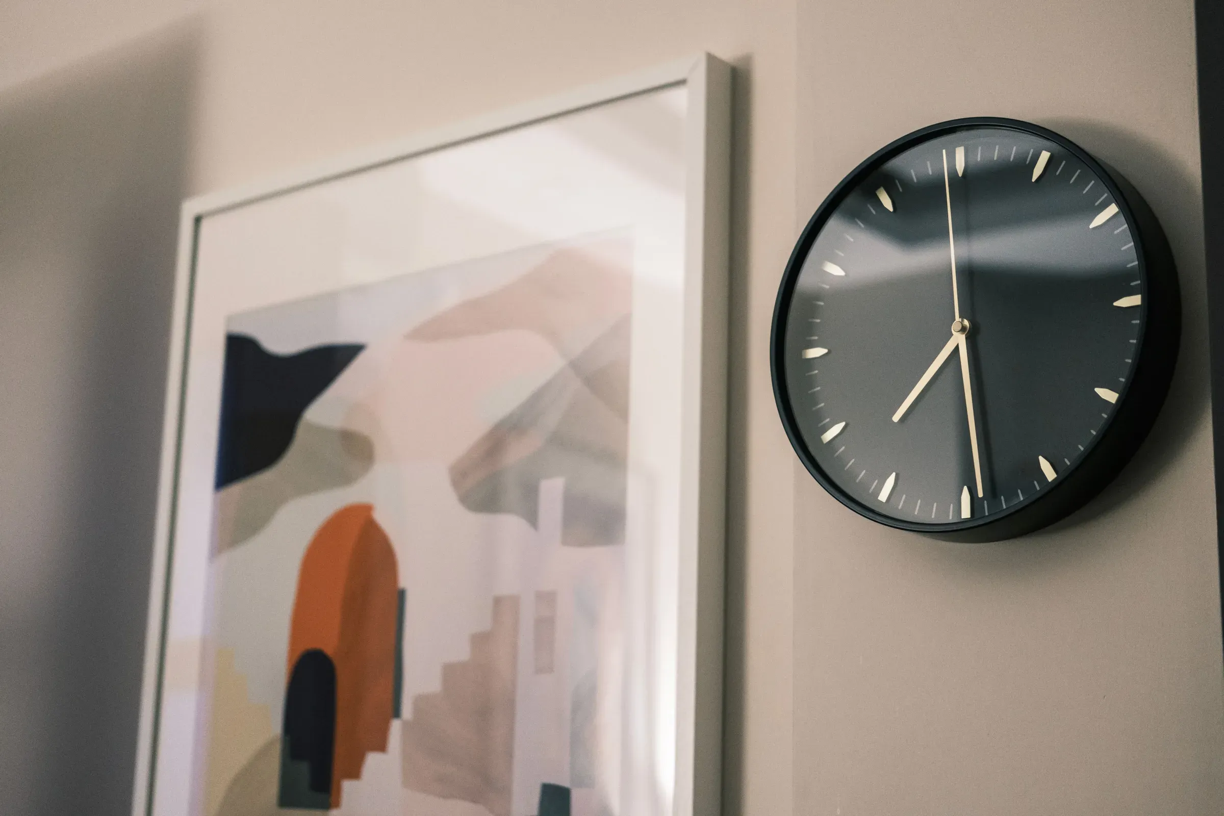 Abstract arch-pattern art print beside a black wall clock on a beige wall