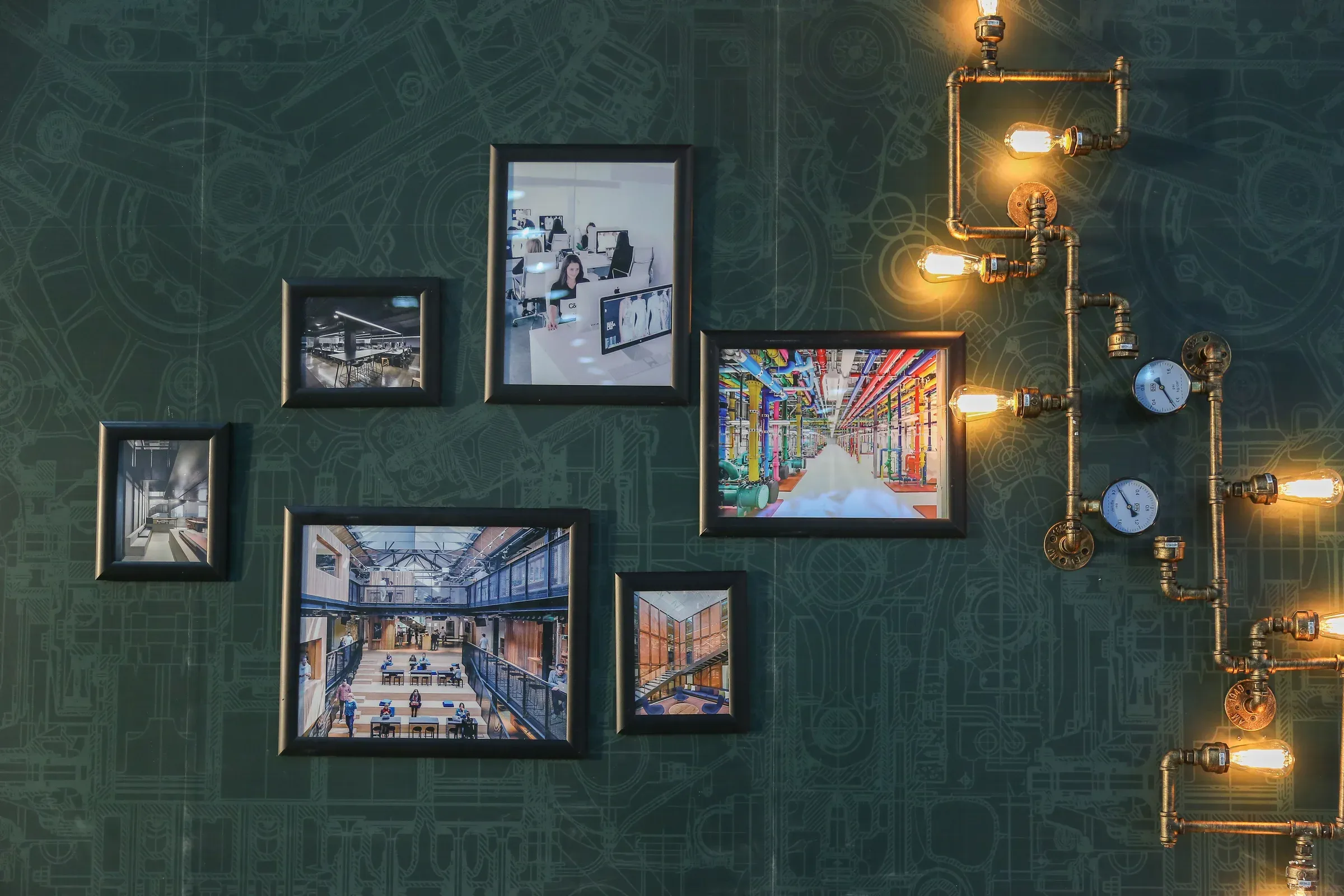 Gallery wall of framed photos on a dark green wall with industrial pipe-and-bulb lights