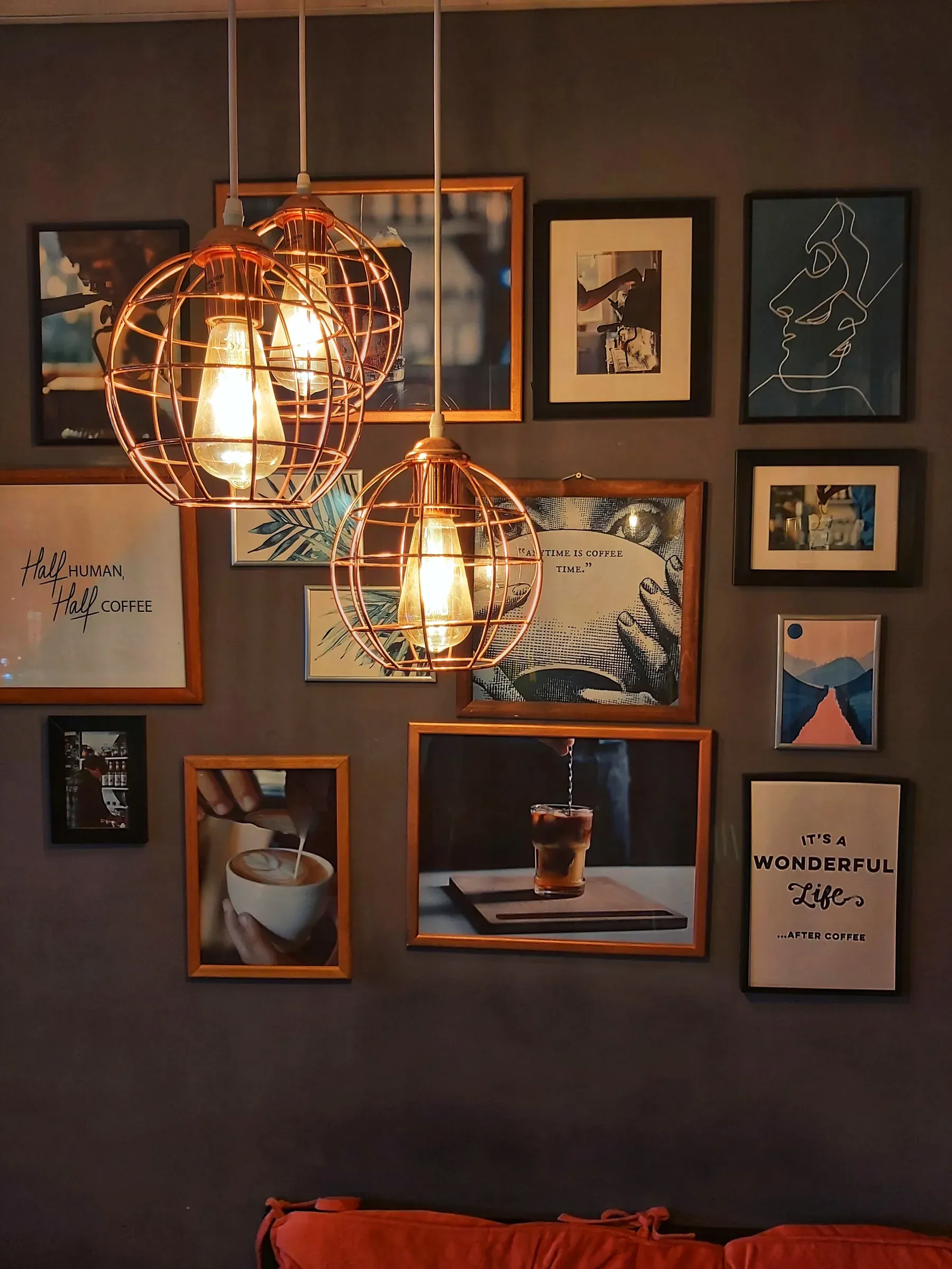 Gallery wall of framed prints on a dark wall with copper cage pendant lights
