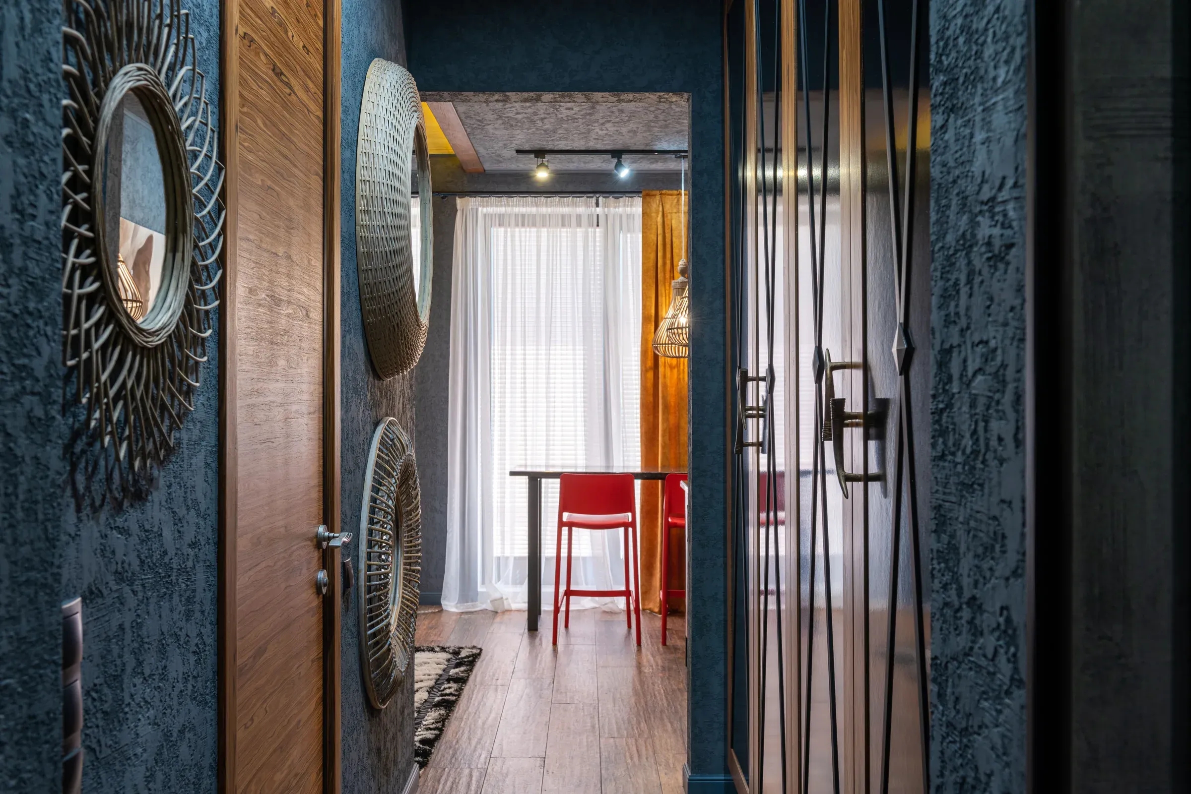 Hallway with sunburst rattan mirrors on a dark blue textured wall, wooden door and a view to the dining area