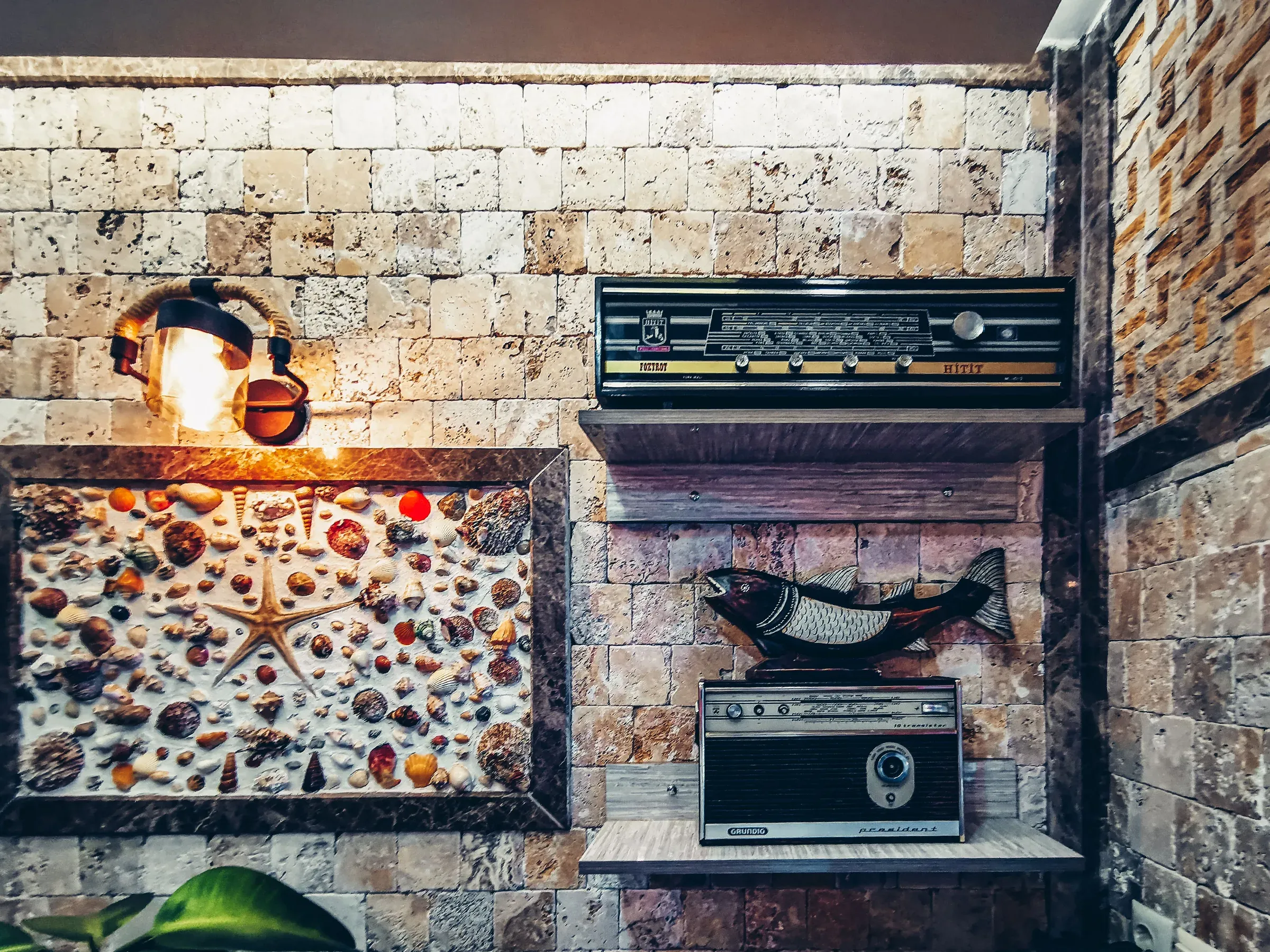 Stone-tile wall with a framed seashell mosaic, vintage radios on shelves and an industrial wall lamp