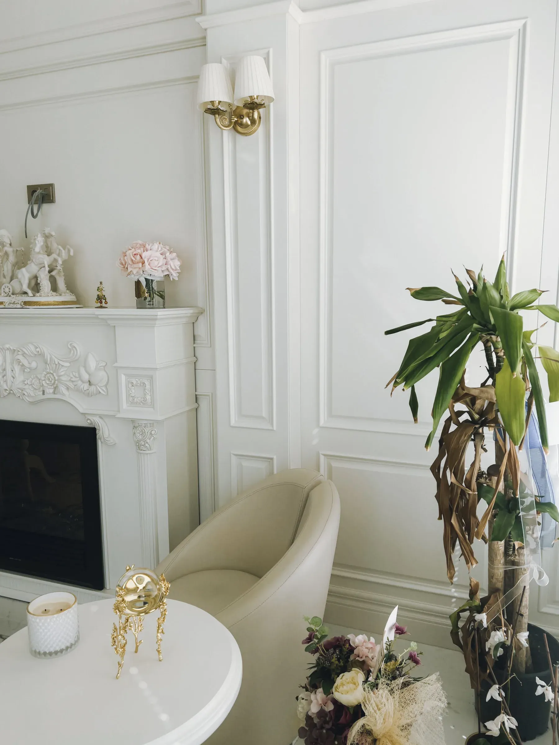 White panelled walls with a carved fireplace, twin-shade wall sconce and cream armchair